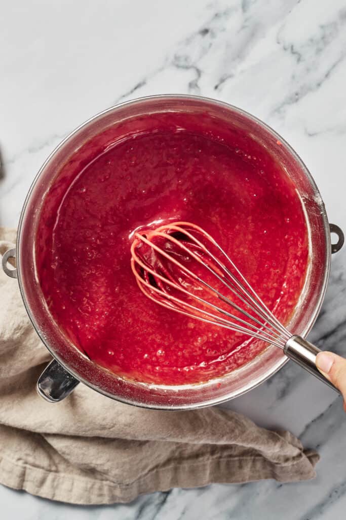 A mixing bowl of red cake batter with a whisk resting in it.