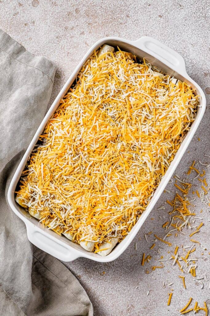 A baking dish with rolled up tortillas and a topping of cheese.