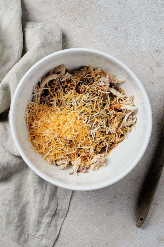A white mixing bowl with chicken, cheese, and other ingredients inside.