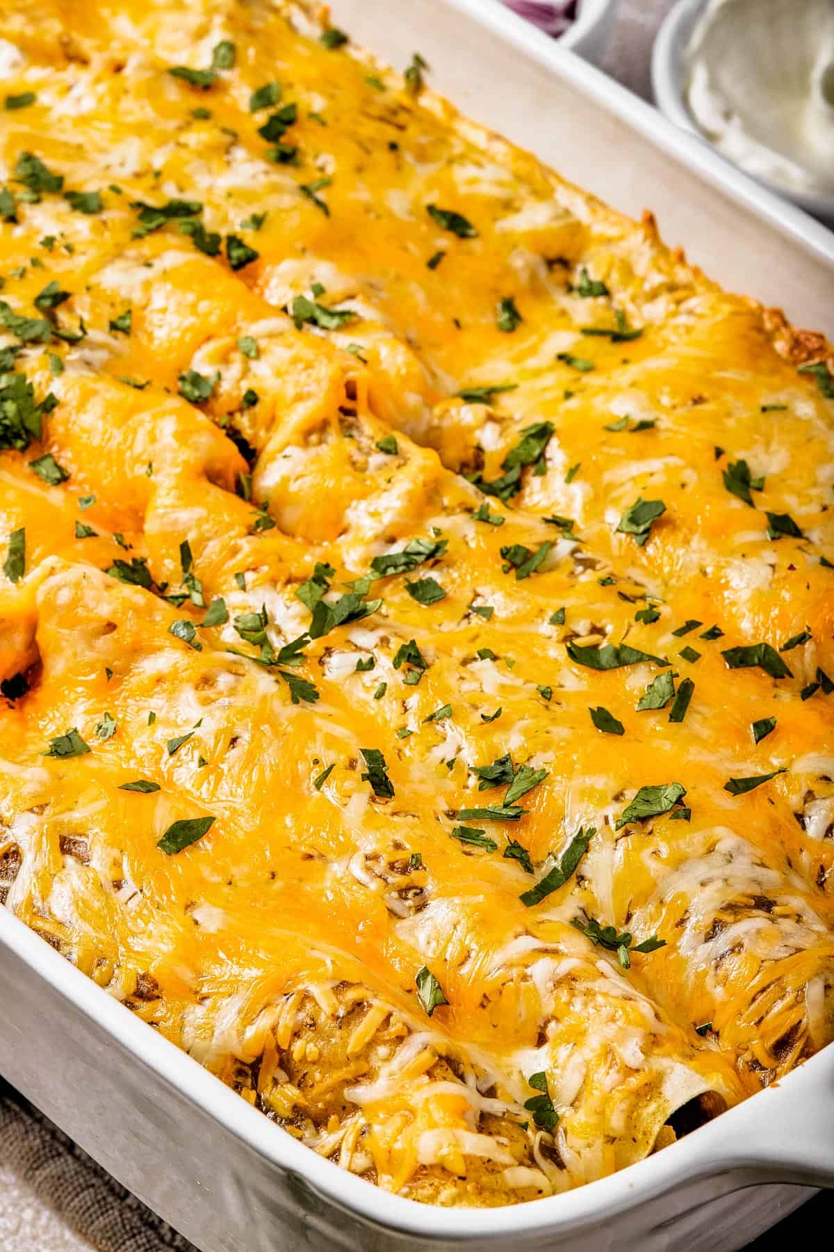 Close-up of a baking dish of cheesy enchiladas, sprinkled with fresh herbs.