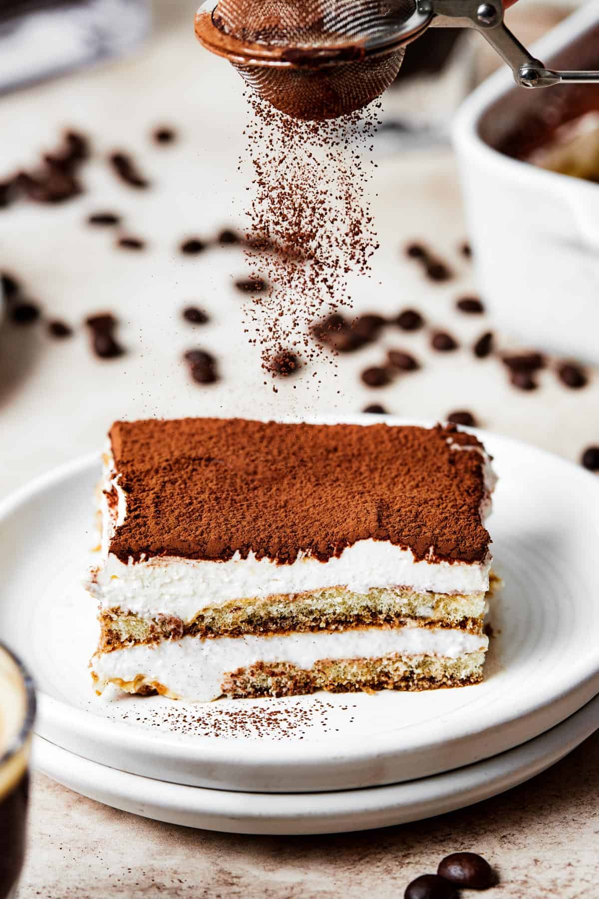 A square of tiramisu on a dessert plate, with the layers visible from the side.
