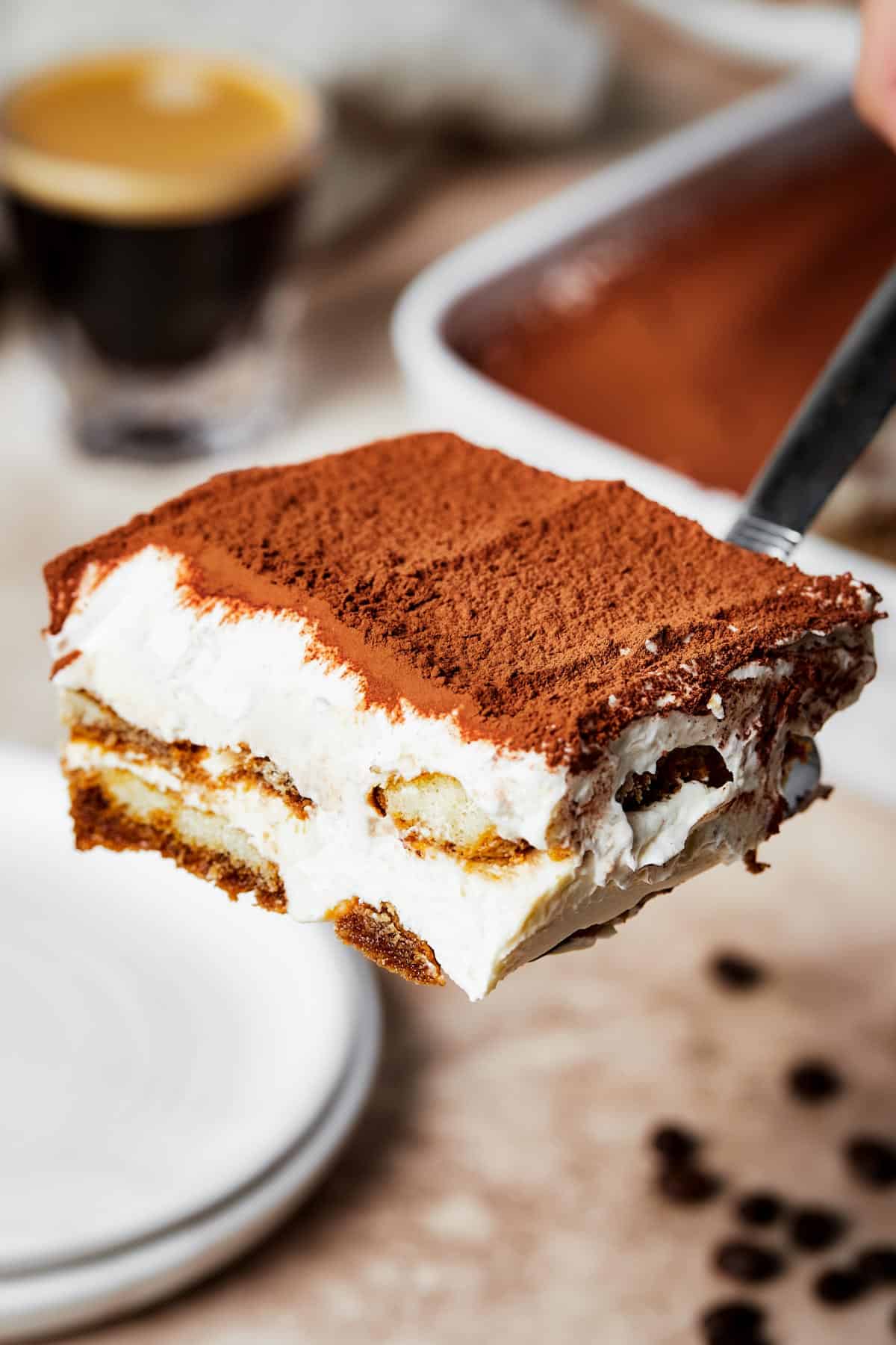A square of tiramisu on a serving utensil being placed on a dessert plate.