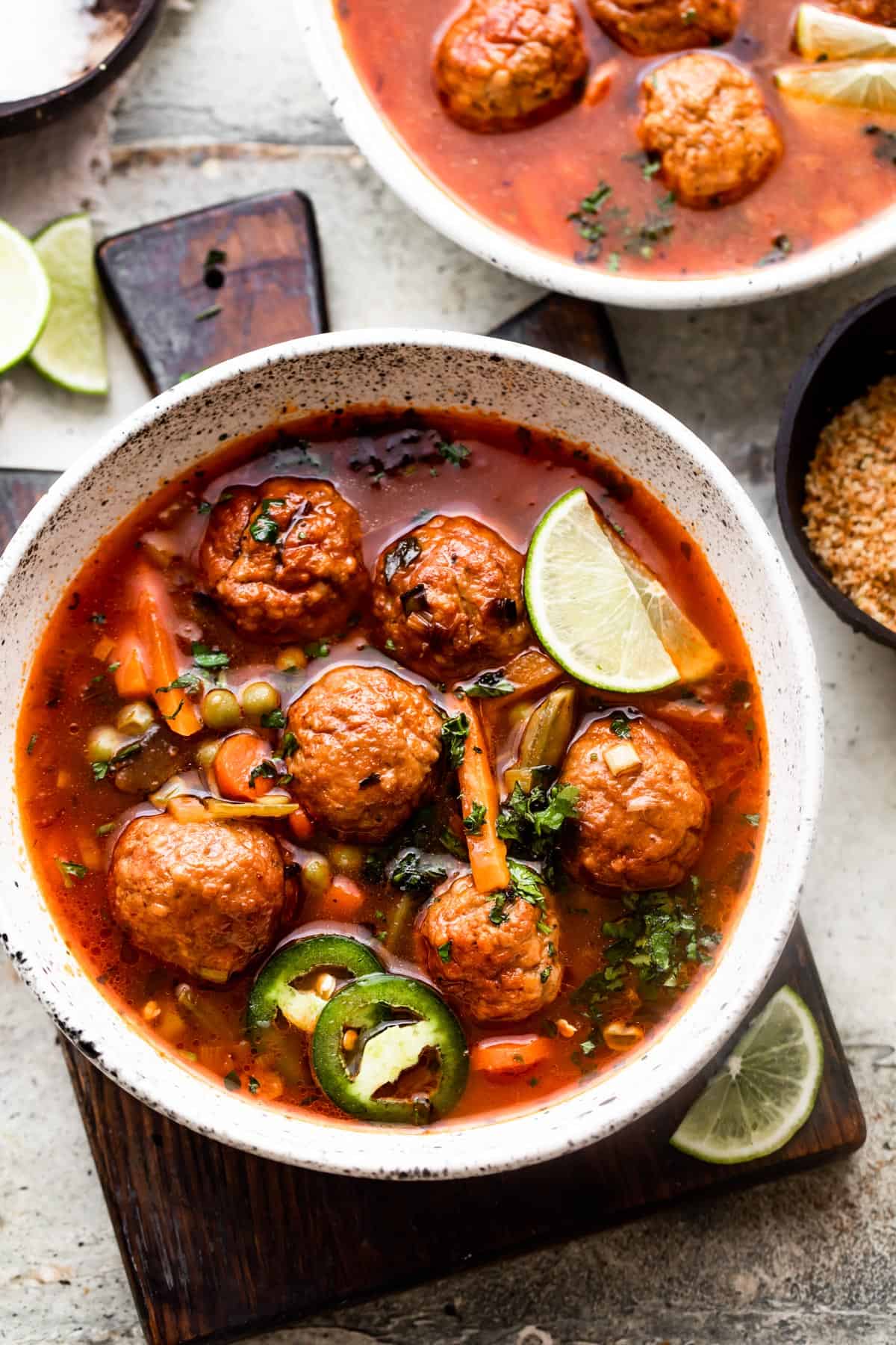 overhead shot of two soup bowls filled with albondigas soup and garnished with limes and sliced jalapenos.