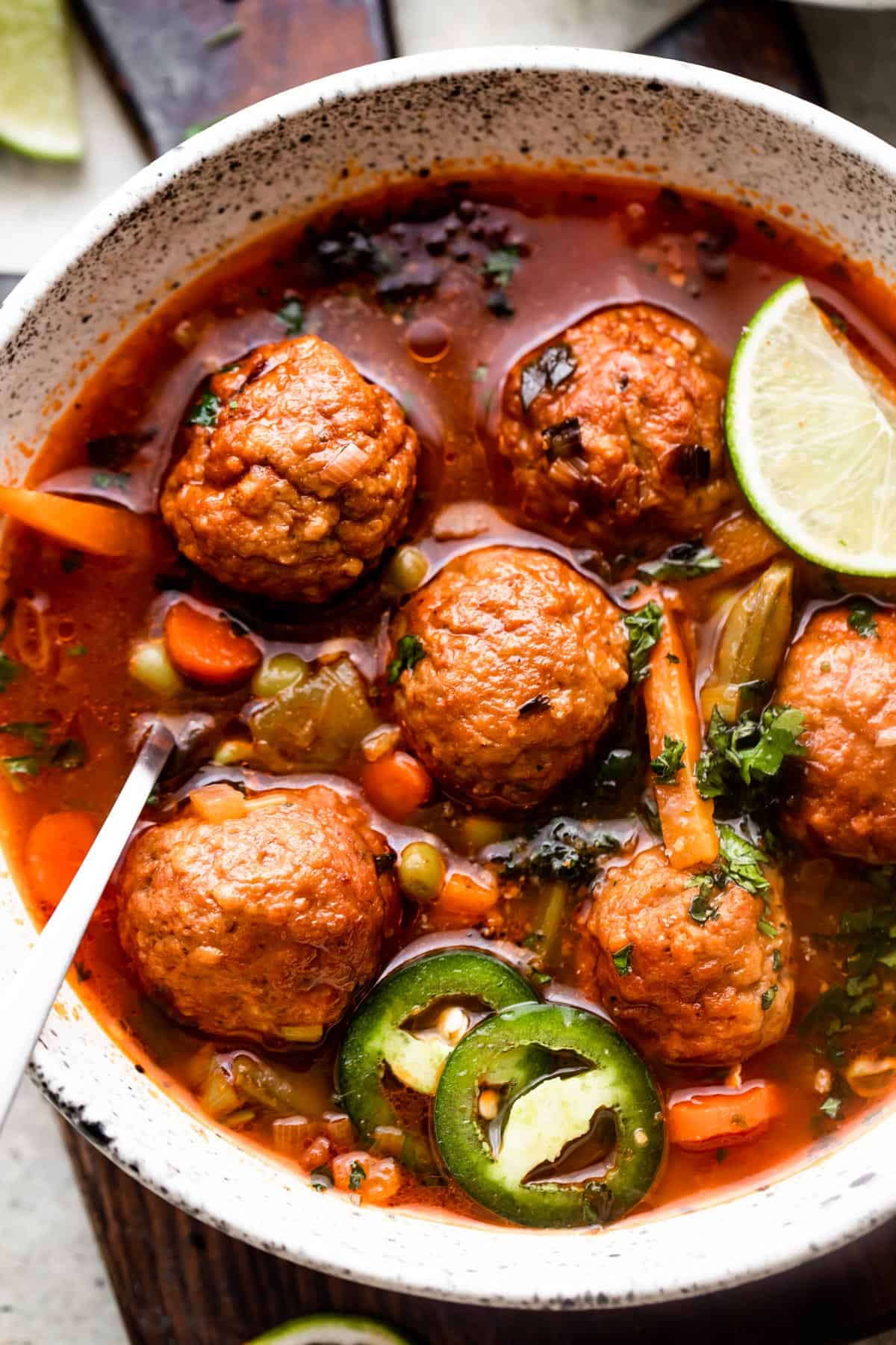 close up overhead shot of soup bowl filled with albondigas soup and garnished with limes and sliced jalapenos.