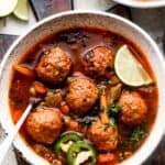 overhead shot of two soup bowls filled with albondigas soup and garnished with limes and sliced jalapenos.