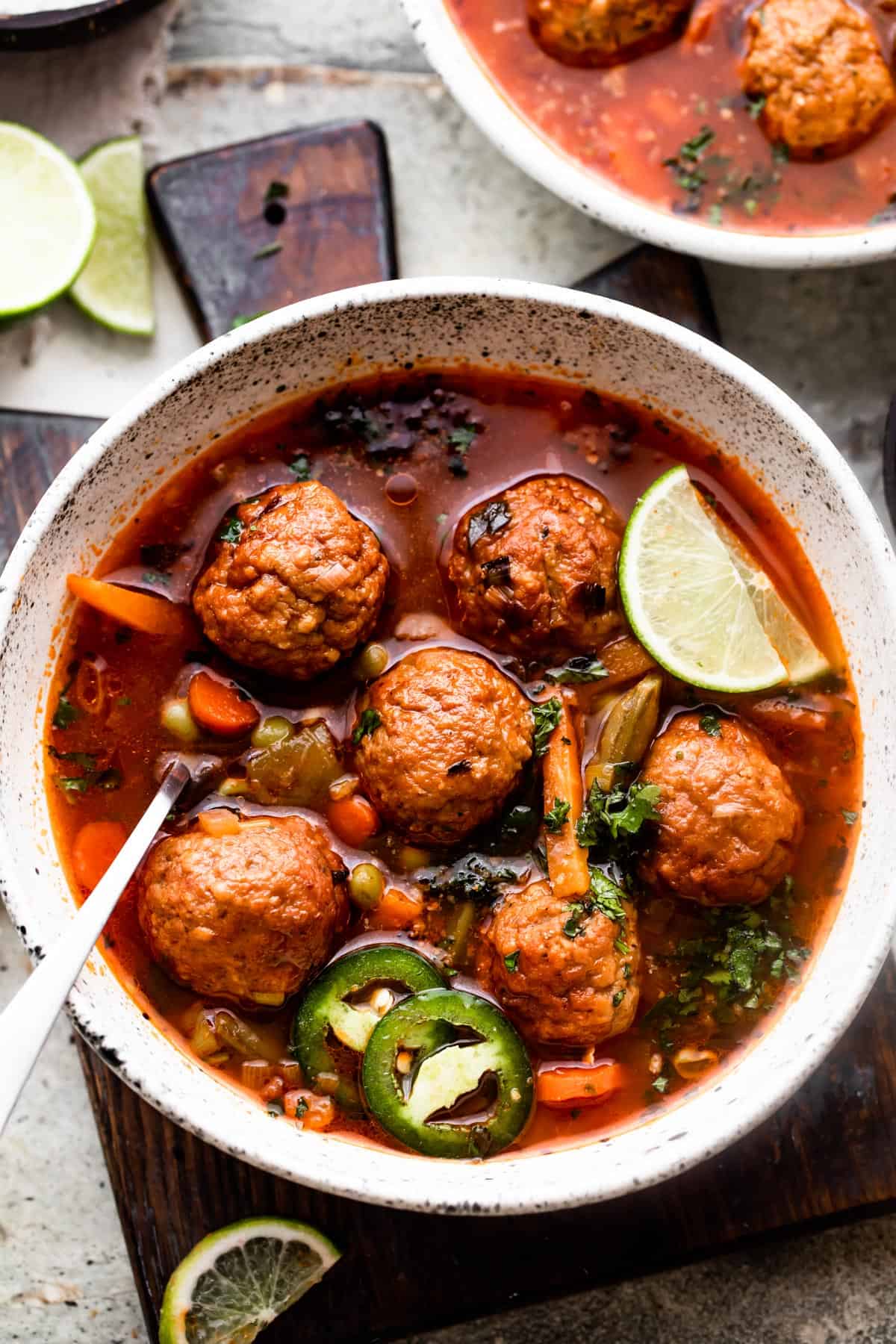 overhead shot of two soup bowls filled with albondigas soup and garnished with limes and sliced jalapenos.