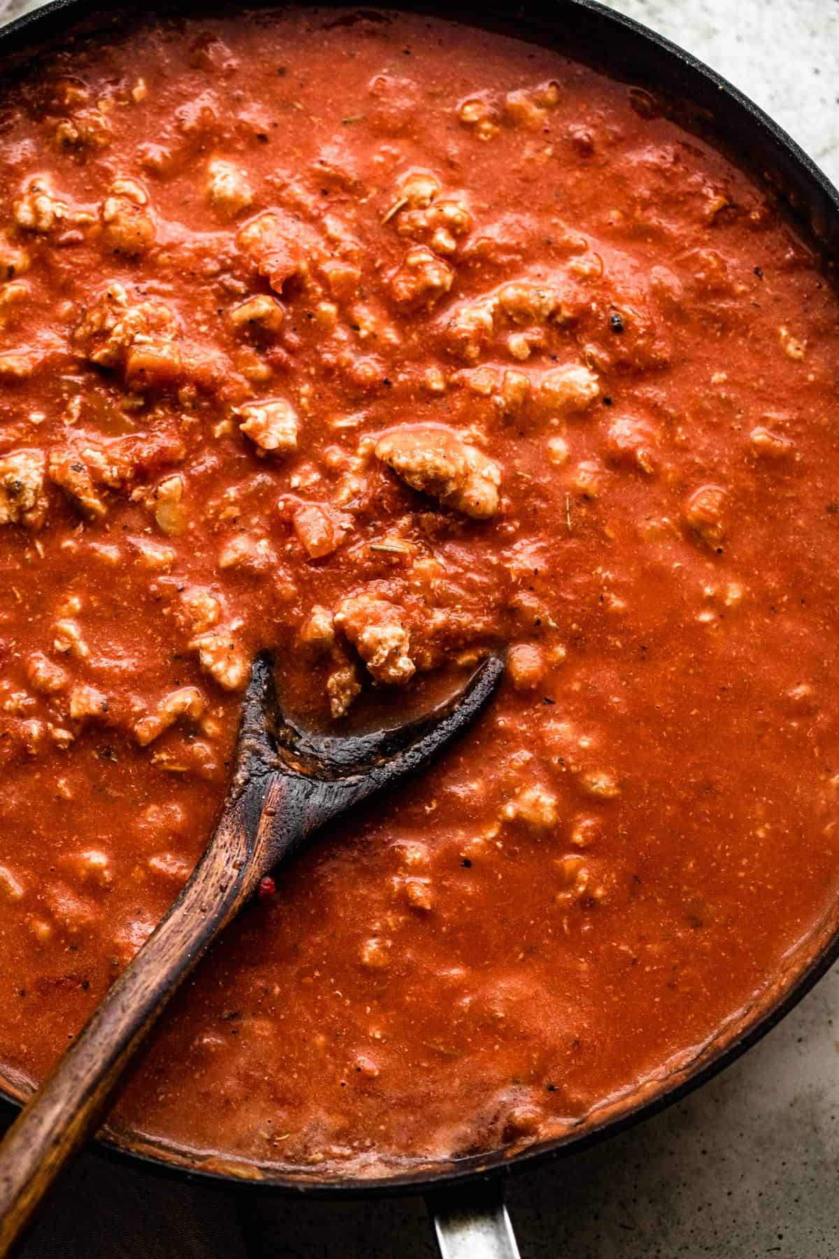 wooden spoon stirring through ground turkey in tomato sauce in a skillet.