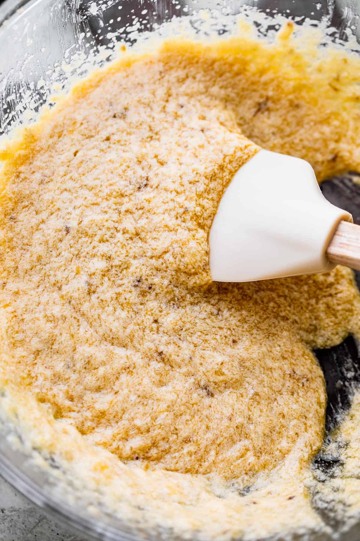 Rubber spatula stirring through liquid batter for banana cookies, showing the texture of the dough.