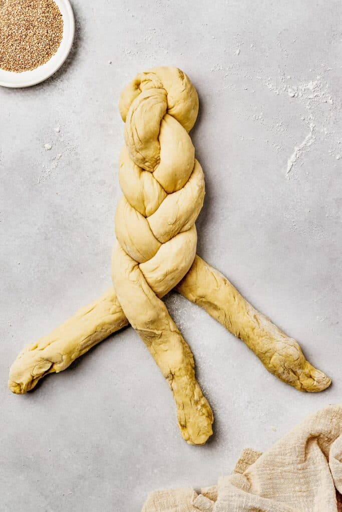 Three long pieces of dough being braided together.