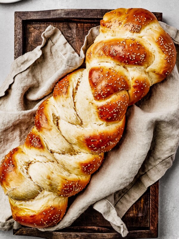 Baked challah with sesame seeds, on a sheet pan with a tea towel.