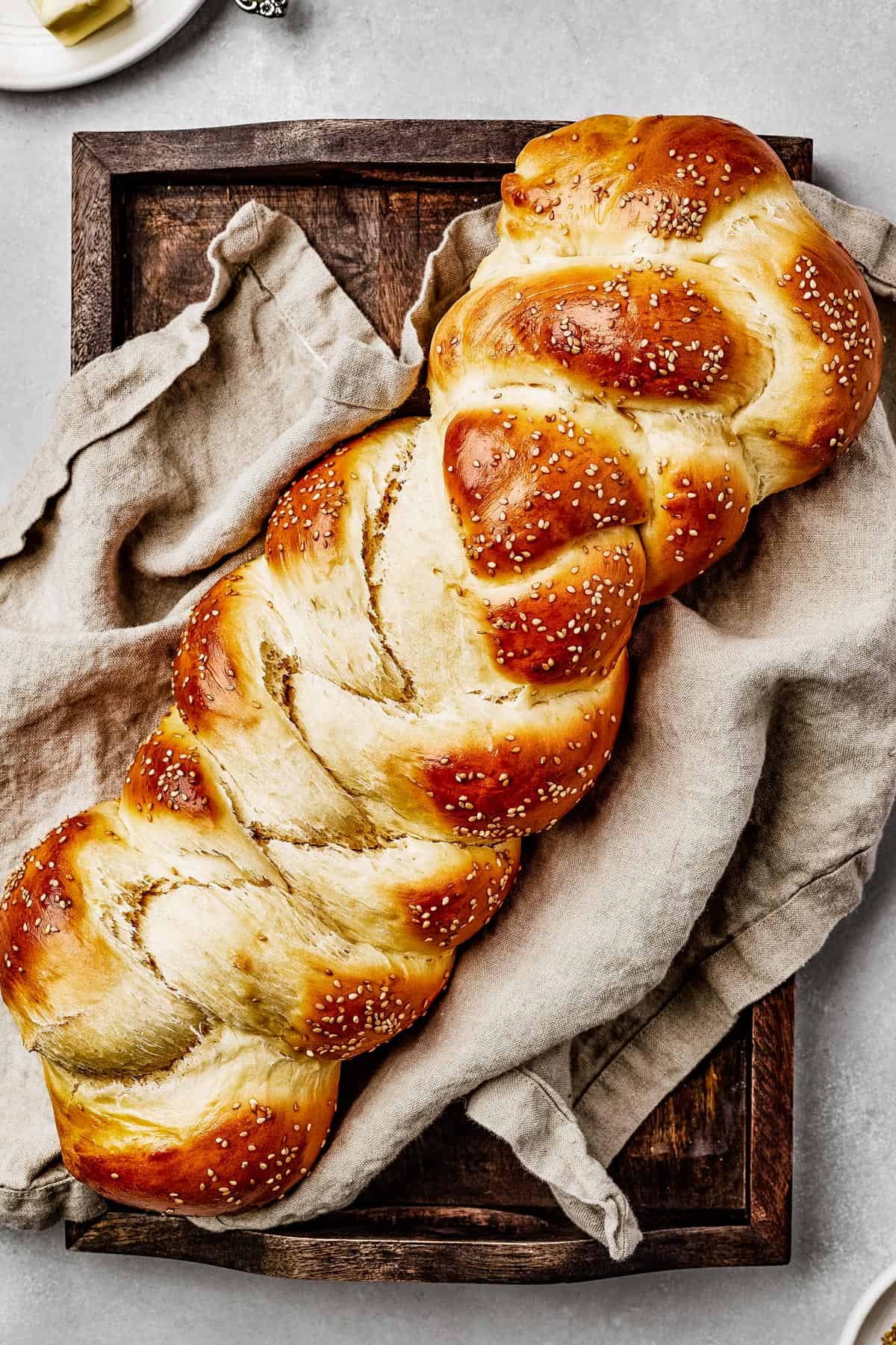 Baked challah with sesame seeds, on a sheet pan with a tea towel.