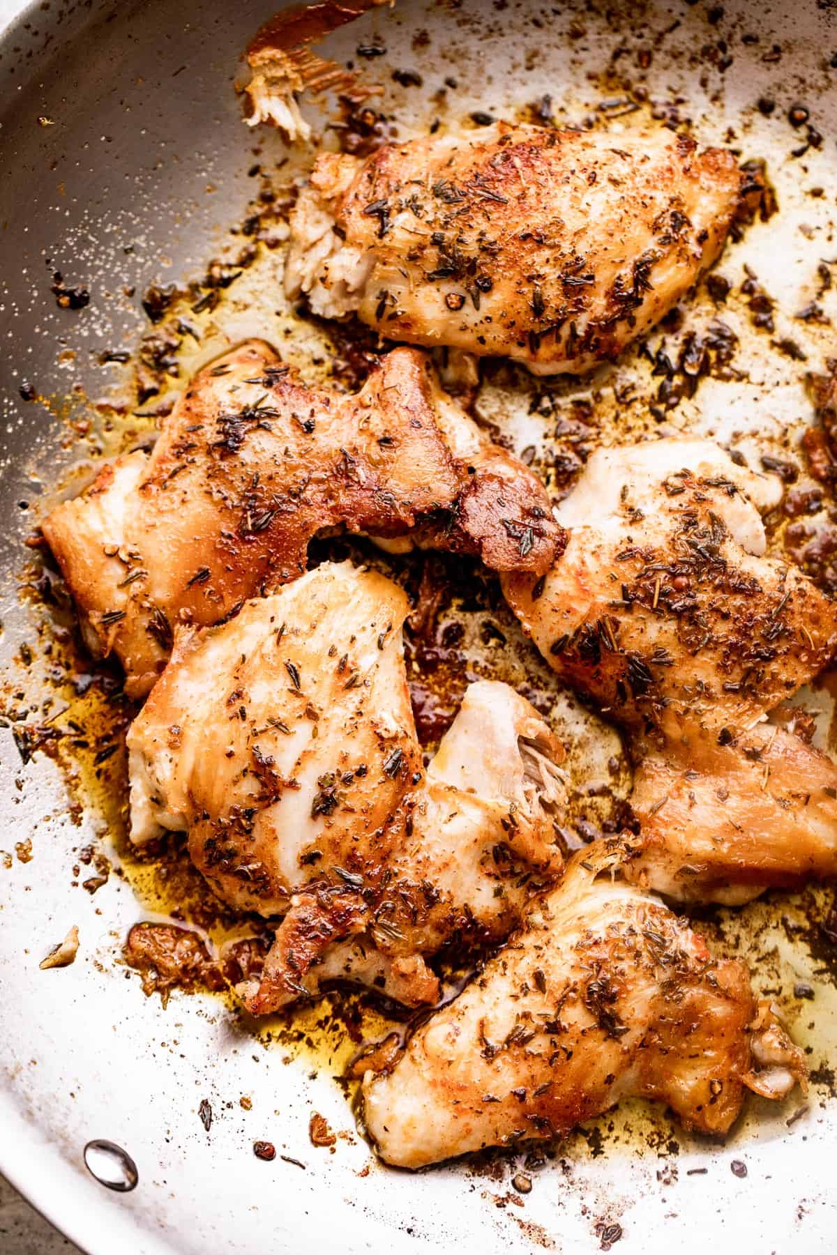 browned boneless chicken thighs seasoned with spices and herbs and set in a skillet.