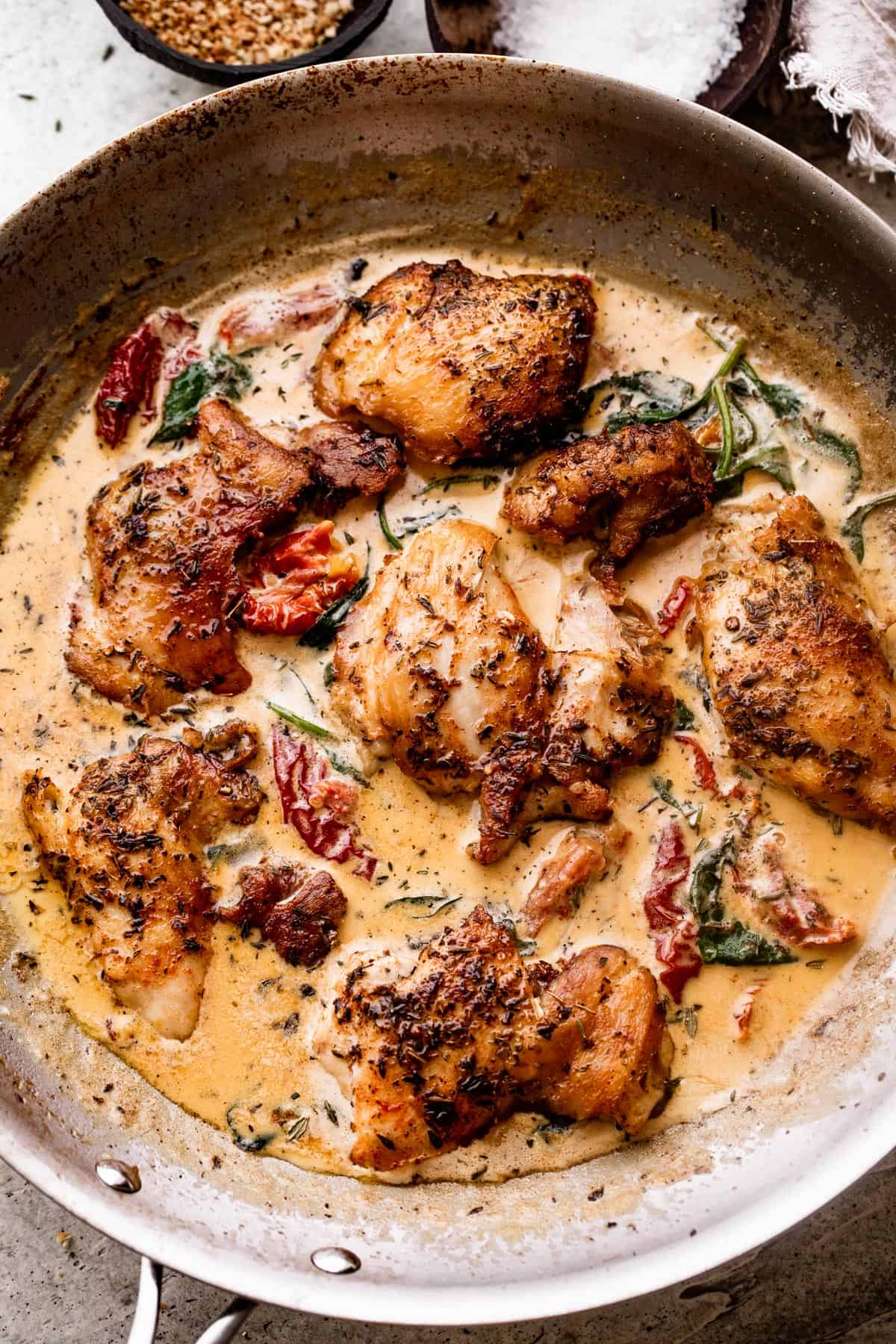 overhead shot of a stainless steel pan with boneless chicken thighs in a creamy sun dried tomato sauce.