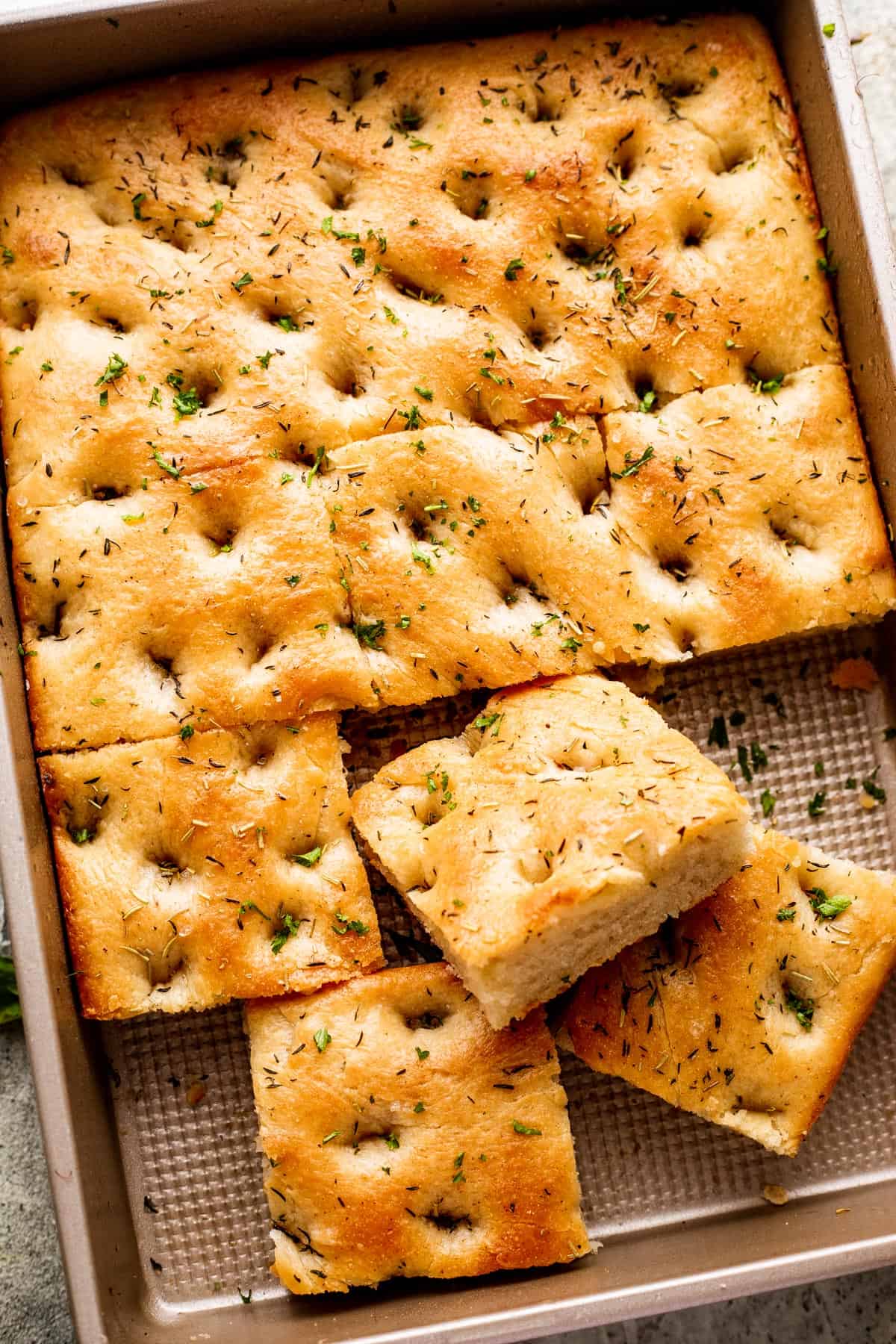 A large pan-sized loaf of focaccia, with four squares of bread cut away.