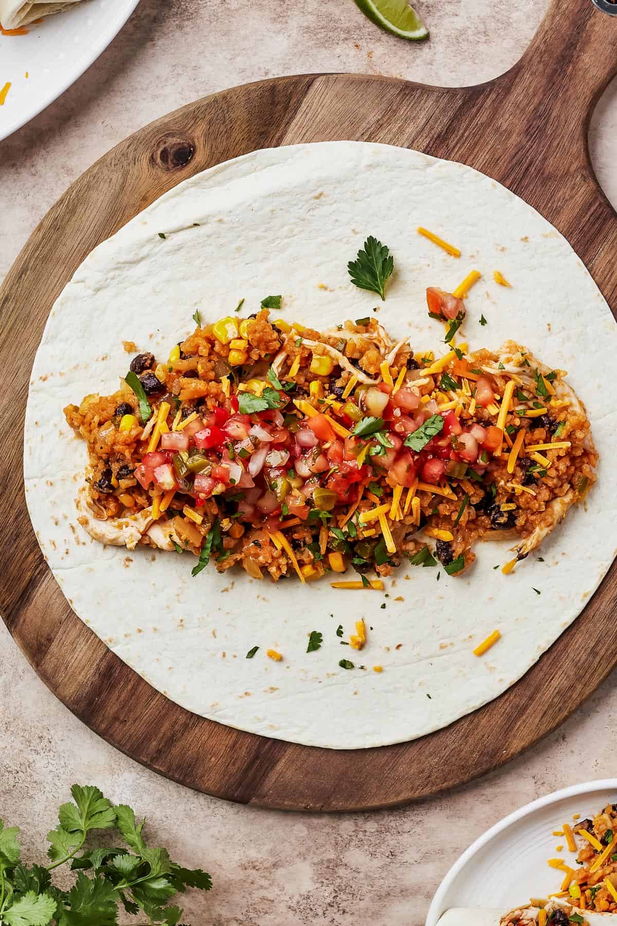 A tortilla on a round wooden cutting board, with chicken filling piled into the center.