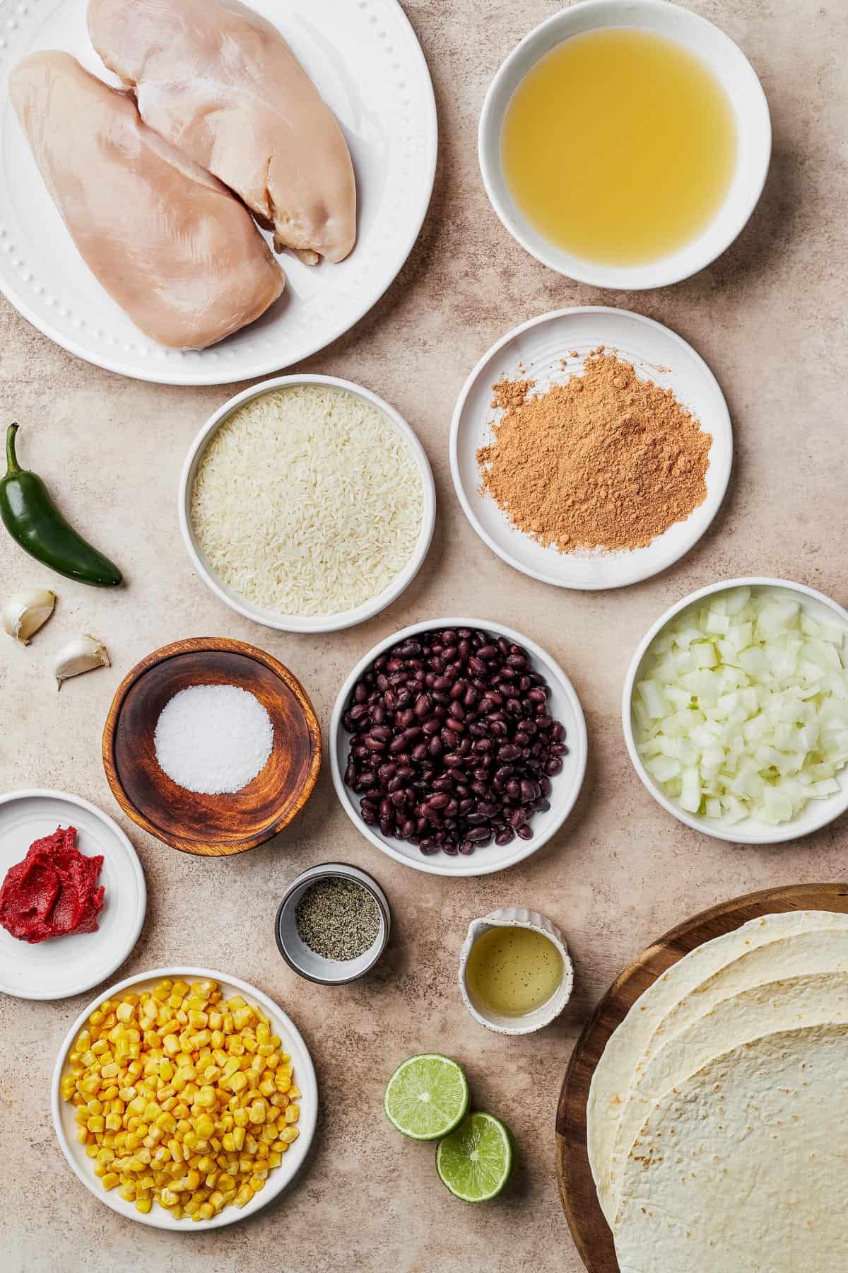 From Top Left: Raw chicken breasts, chicken broth, jalapeno, garlic, rice, taco seasoning, salt, black beans, chopped onions, tomato paste, pepper, lime juice, corn, lime halves, tortillas.