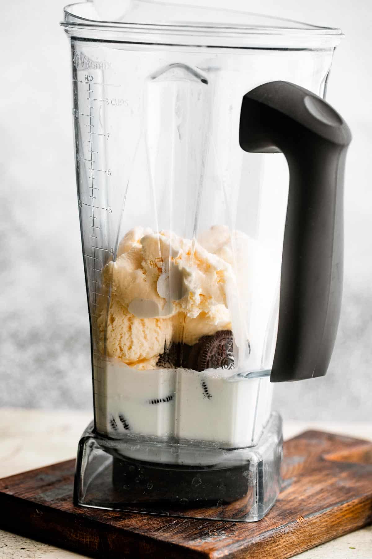 jar of a blender filled with milk, heavy cream, ice cream, and oreo cookies.