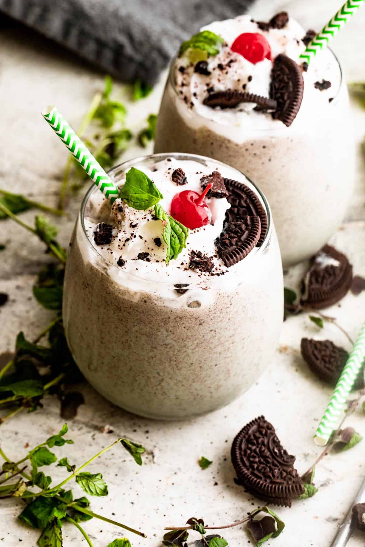 two drinking glasses filled with Shamrock Oreo McFlurry Shake, topped with whipped cream, maraschino cherries, and mint leaves.
