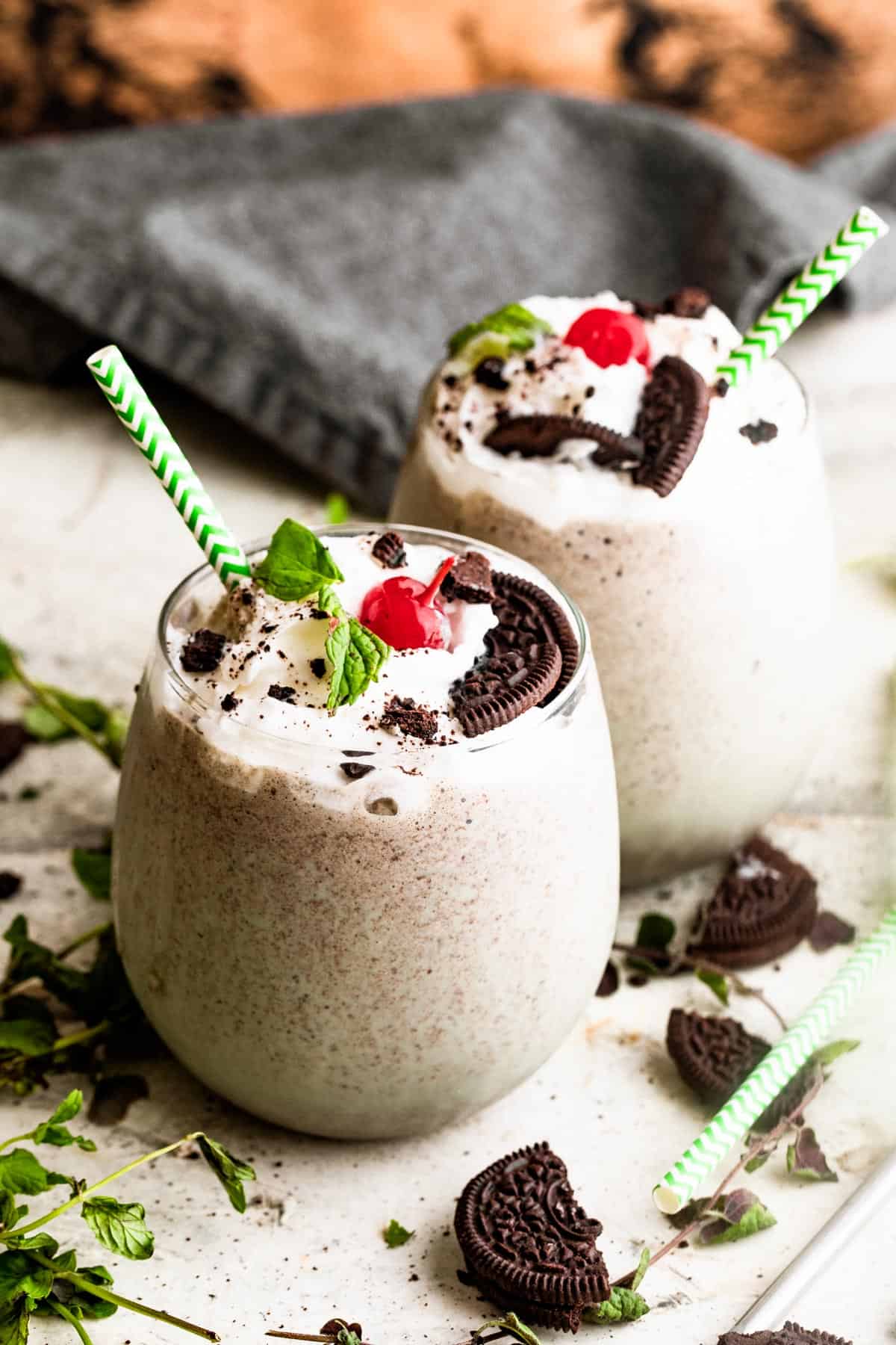 two drinking glasses filled with Shamrock Oreo McFlurry Shake, topped with whipped cream, maraschino cherries, and mint leaves.