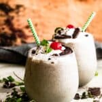 two drinking glasses filled with Shamrock Oreo McFlurry Shake, topped with whipped cream, maraschino cherries, and mint leaves.