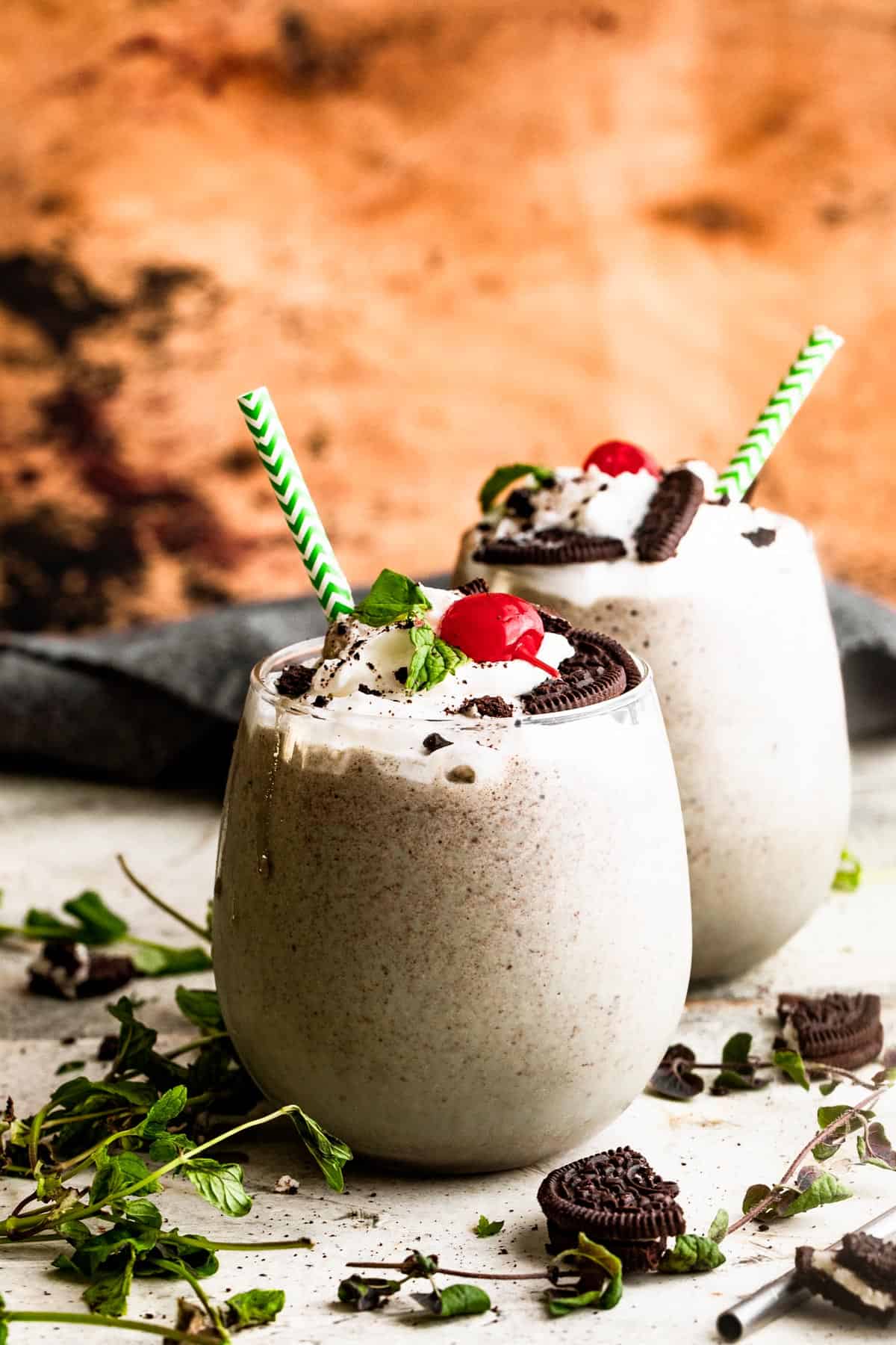 two drinking glasses filled with Shamrock Oreo McFlurry Shake, topped with whipped cream, maraschino cherries, and mint leaves.