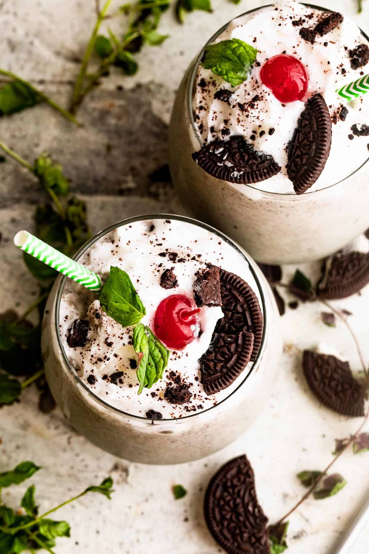 two drinking glasses filled with Shamrock Oreo McFlurry Shake, topped with whipped cream, maraschino cherries, and mint leaves.