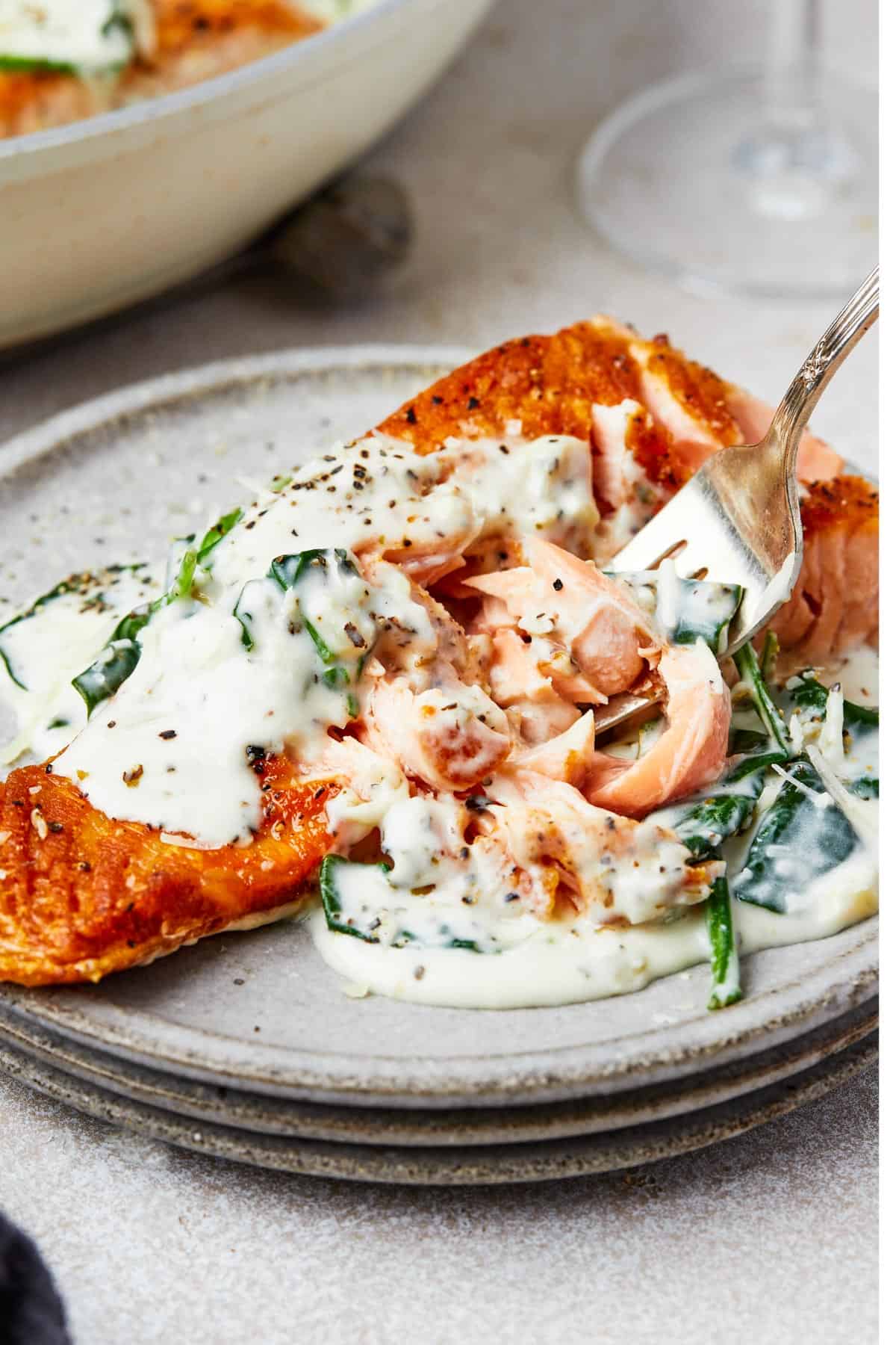 A serving of salmon florentine. A bite of the salmon is being lifted toward the camera on a fork.