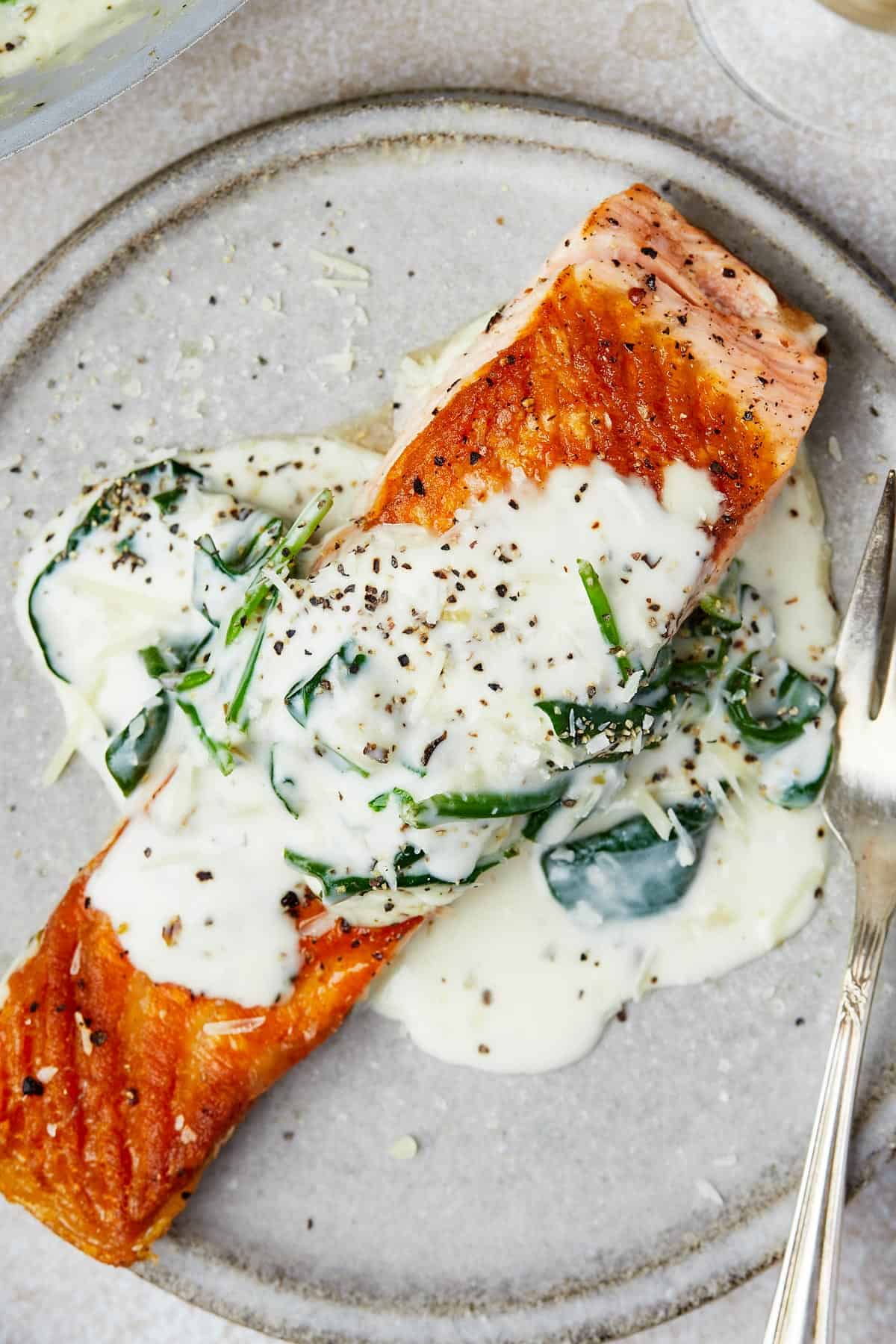 A salmon fillet topped with creamy sauce on a small plate.