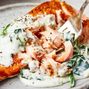 A serving of salmon florentine. A bite of the salmon is being lifted toward the camera on a fork.
