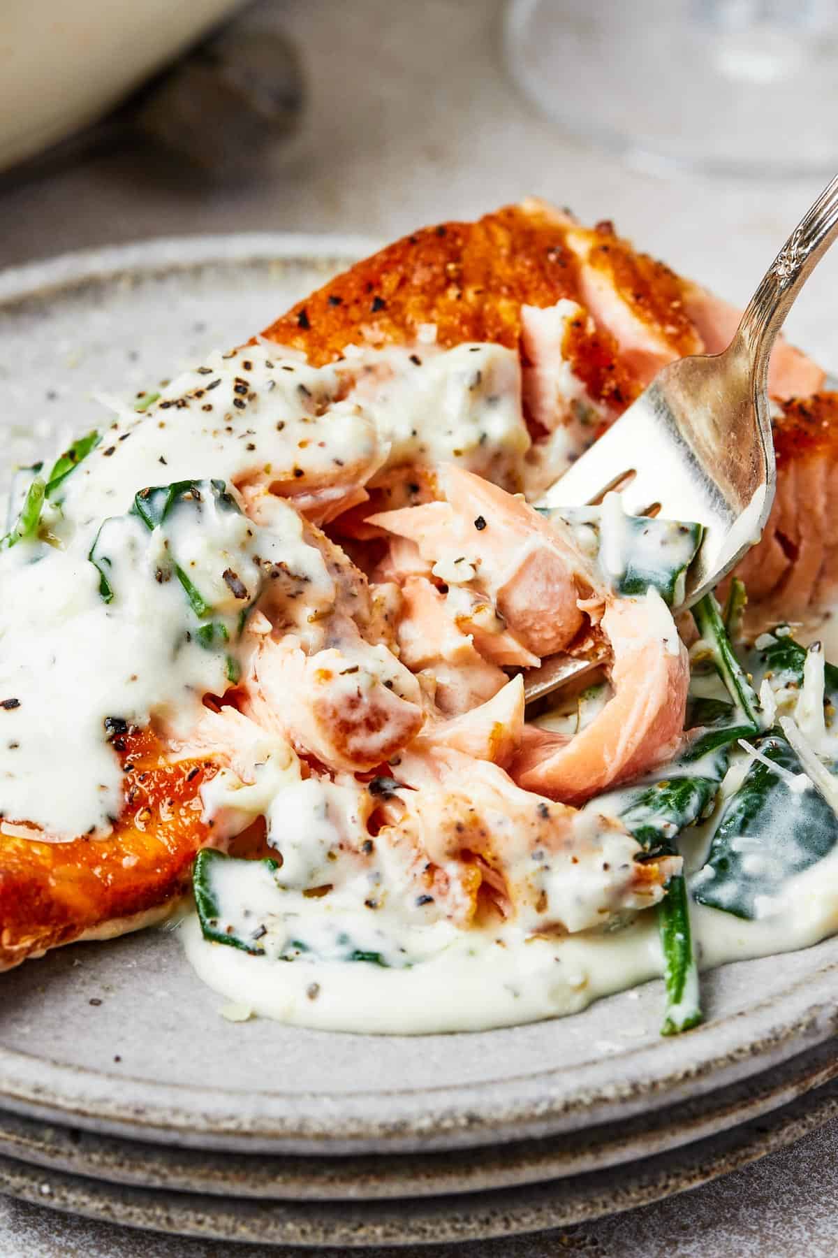 A serving of salmon florentine. A bite of the salmon is being lifted toward the camera on a fork.