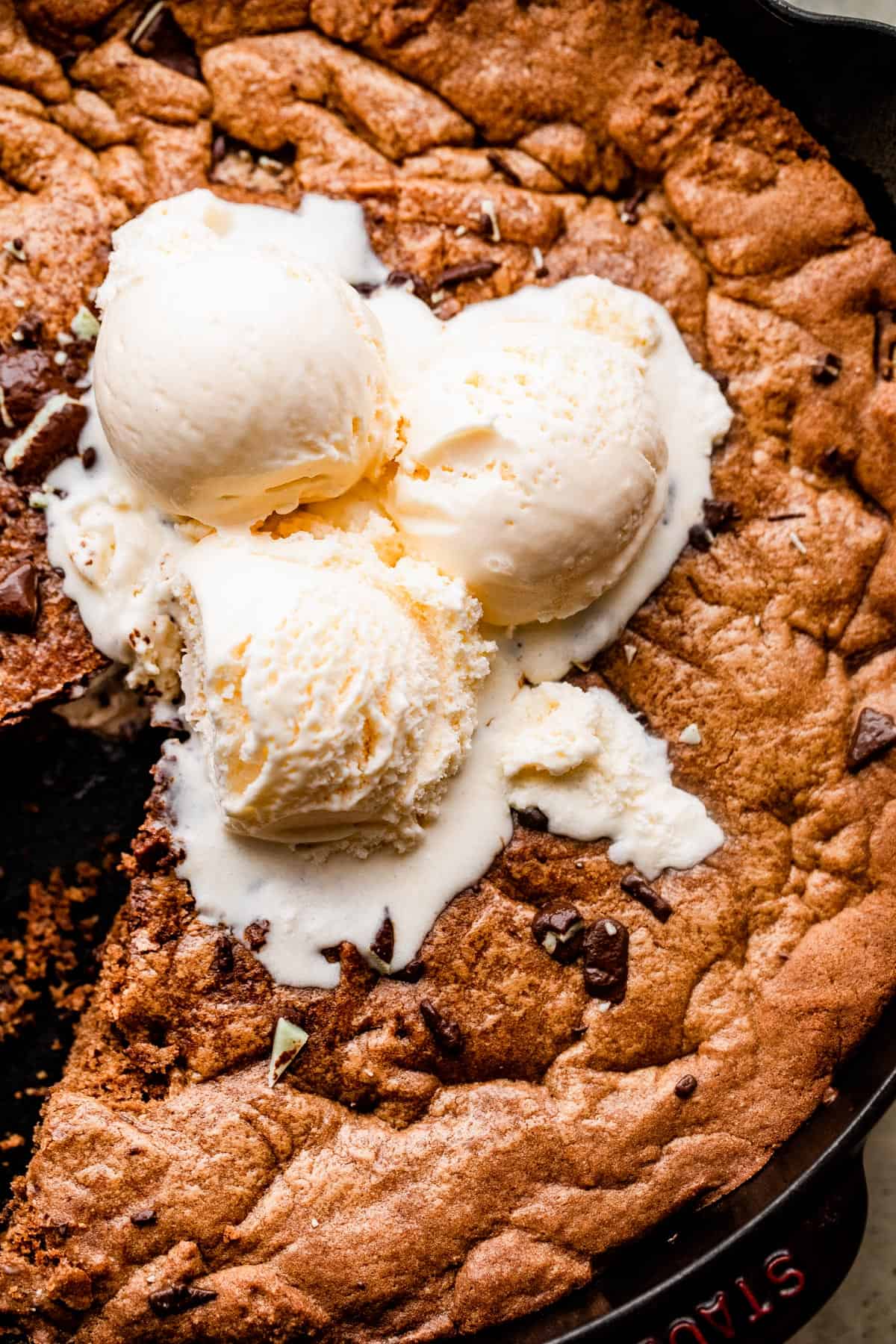 close up overhead shot of three vanilla ice cream scoops set on top of a large skillet cookie.