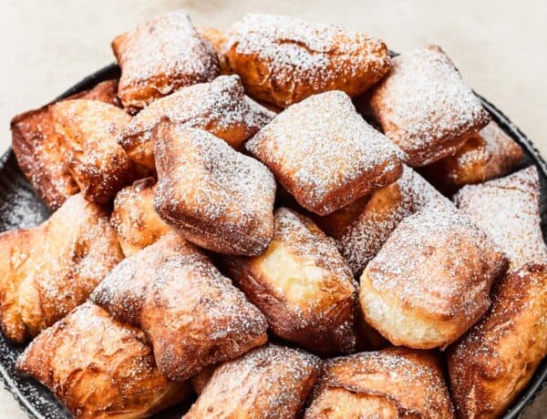 A plate of fried beignets, dusted with powdered sugar.
