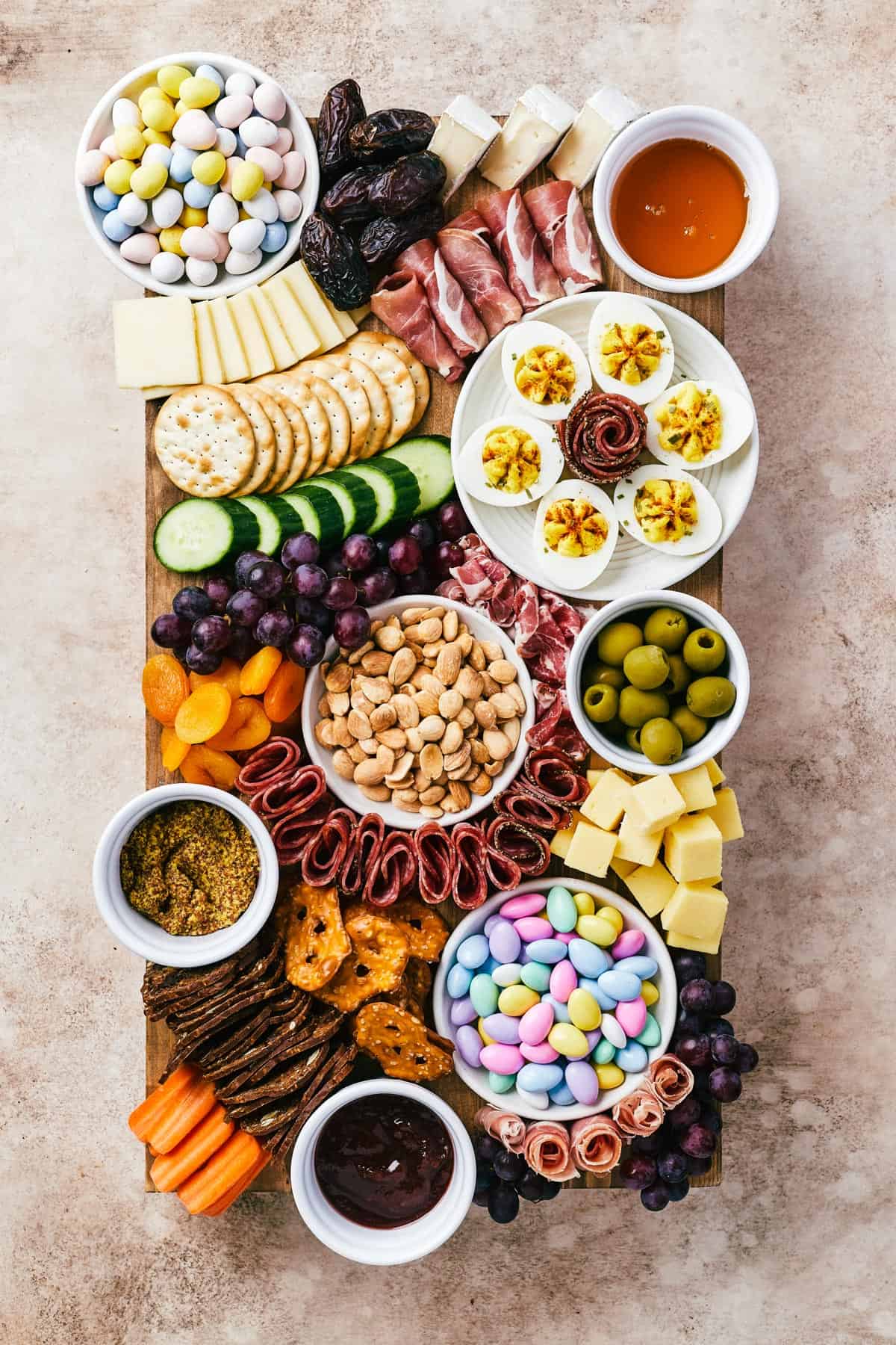 A wooden cutting board artistically arranged with meats, cheeses, crackers, olives, fruit, veggies, and more.