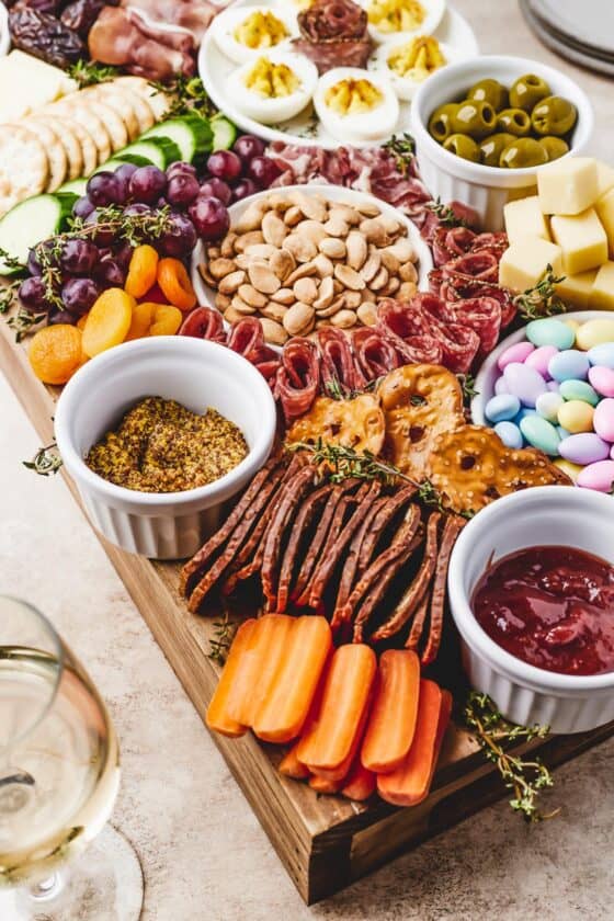 Close-up shot of a cutting board arranged with marcona almonds, grapes, dried apricots, baby carrots, fig crackers, and more.