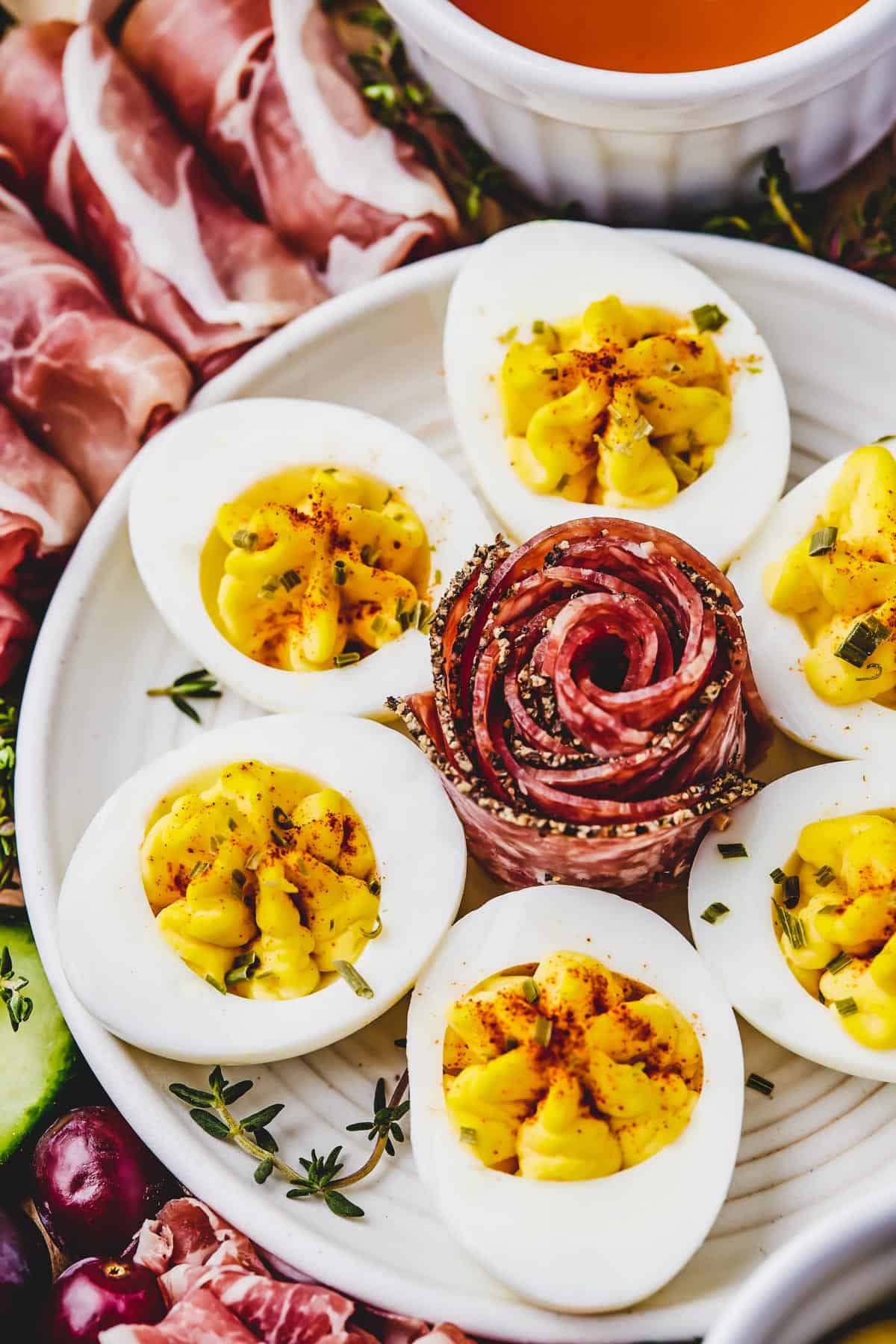 Close-up shot of a plate of deviled eggs with an artistically folded slice of coppa in the center.