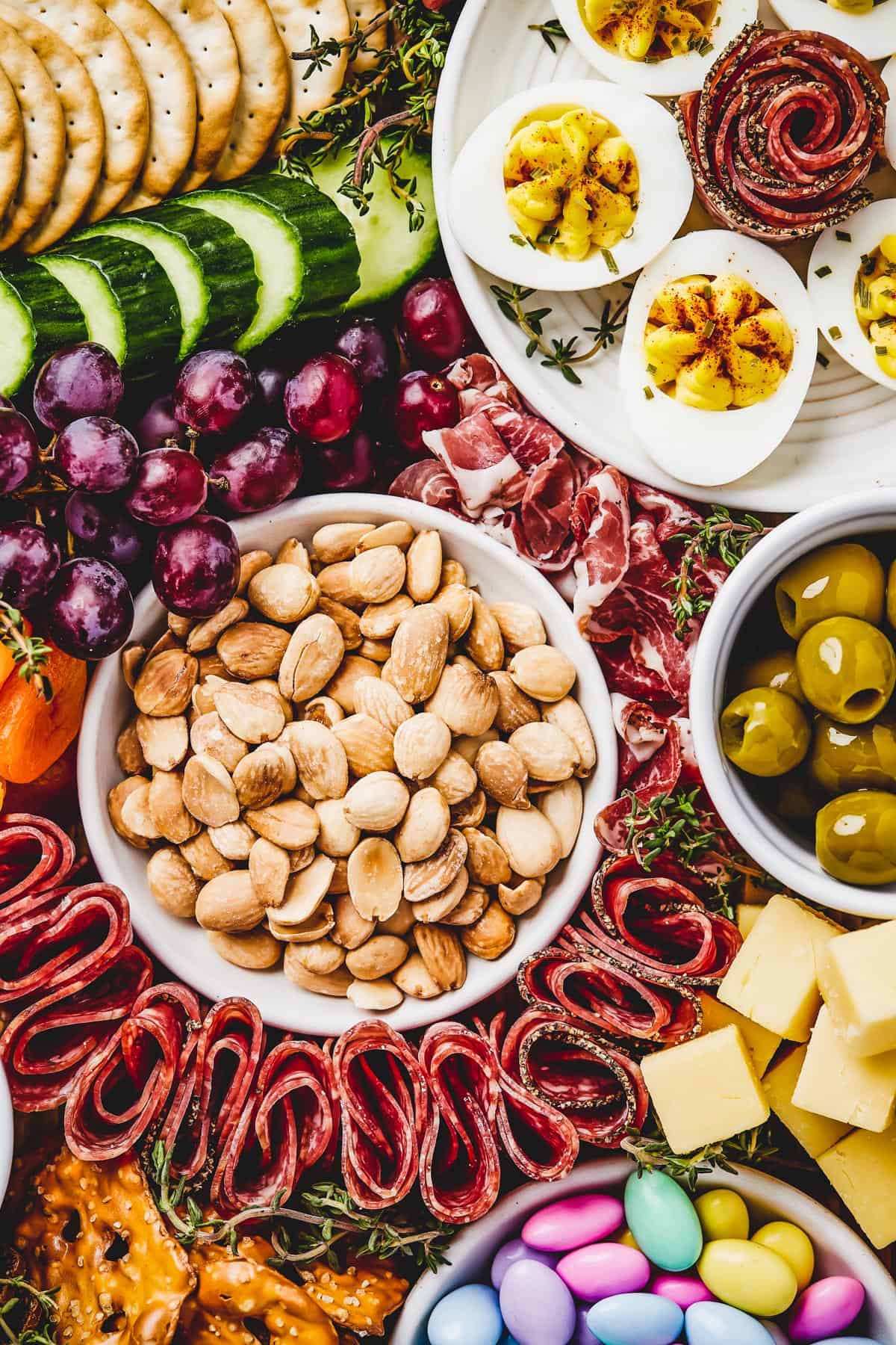 Close-up shot of marcona almonds in a dish, surrounded by folded salami, dried apricots, red grapes, olives, and more.