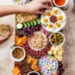 A wooden cutting board artistically arranged with meats, cheeses, crackers, olives, fruit, veggies, and more.