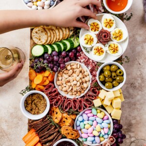 A wooden cutting board artistically arranged with meats, cheeses, crackers, olives, fruit, veggies, and more.