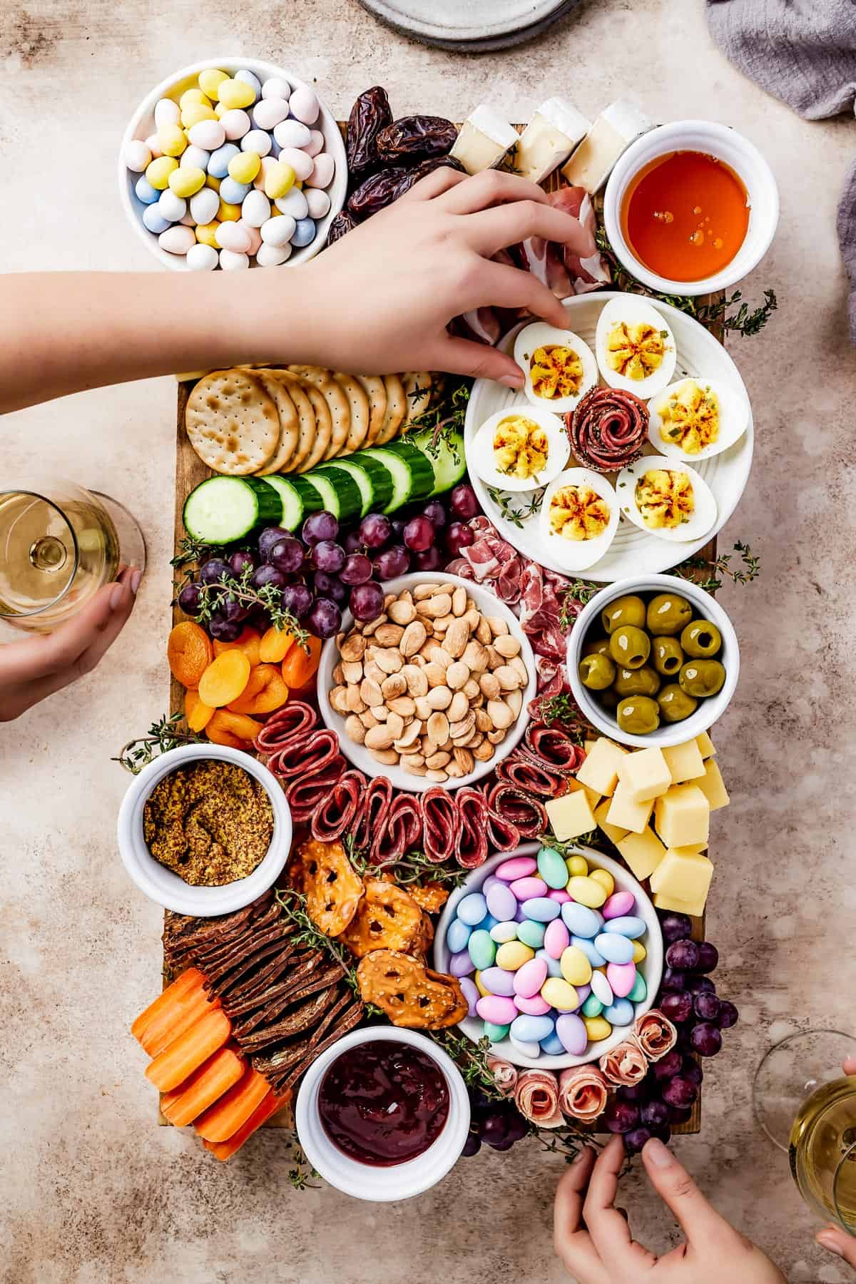 A wooden cutting board artistically arranged with meats, cheeses, crackers, olives, fruit, veggies, and more.