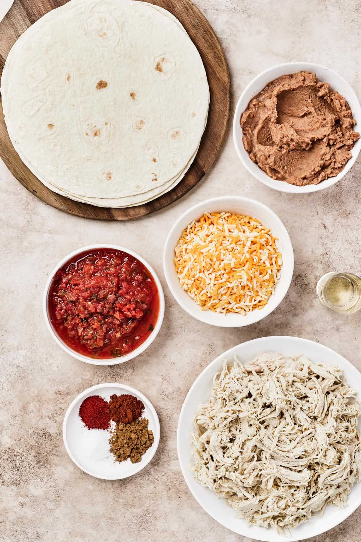 From top left: Tortillas, refried beans, salsa, shredded cheese, oil, spices, shredded chicken.