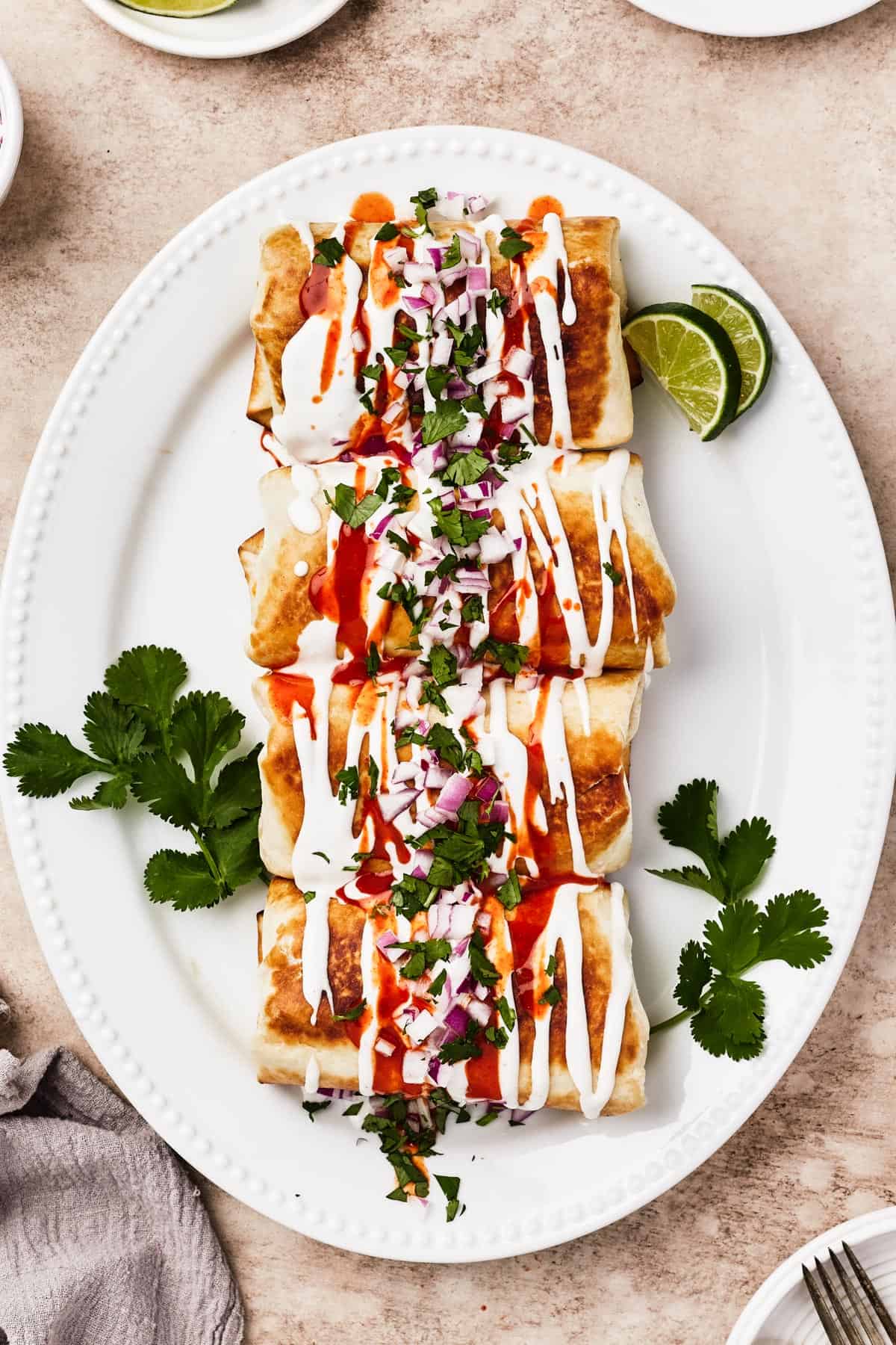 A plate of fried chimichangas, garnished with sour cream, hot sauce, cilantro, lime, and chopped red onion.