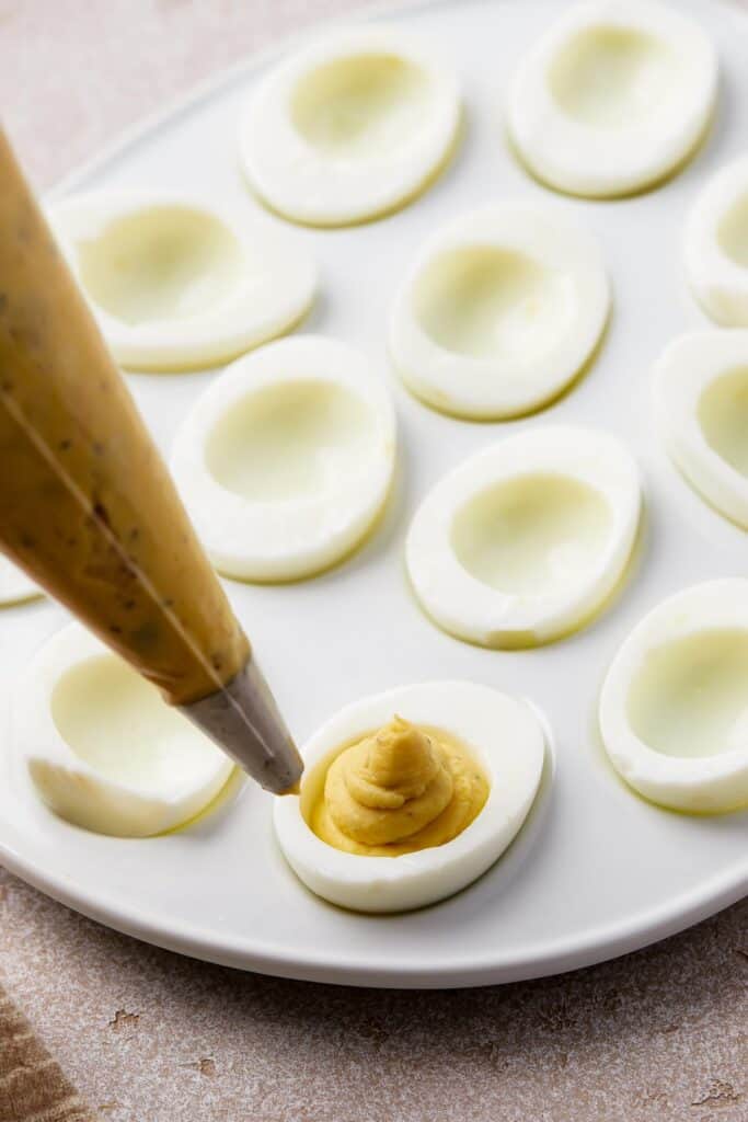 Creamy, yellow filling being piped into hard-boiled egg whites.