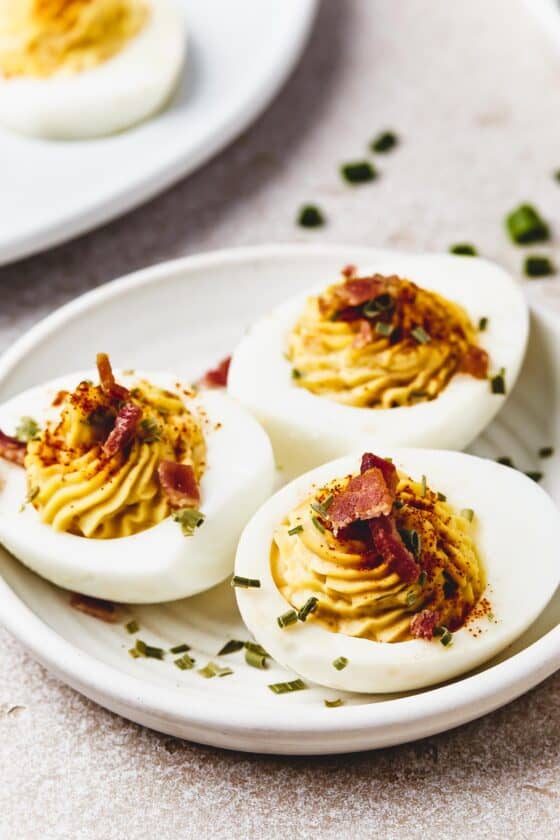 A small dish with three stuffed egg halves on it, sprinkled with chives, paprika, and bacon.
