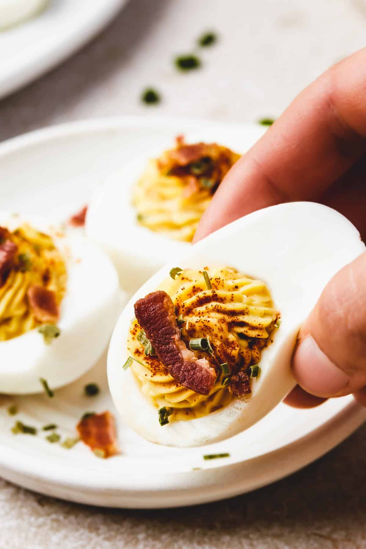 A woman's hand is lifting a deviled egg from a small plate toward the camera.