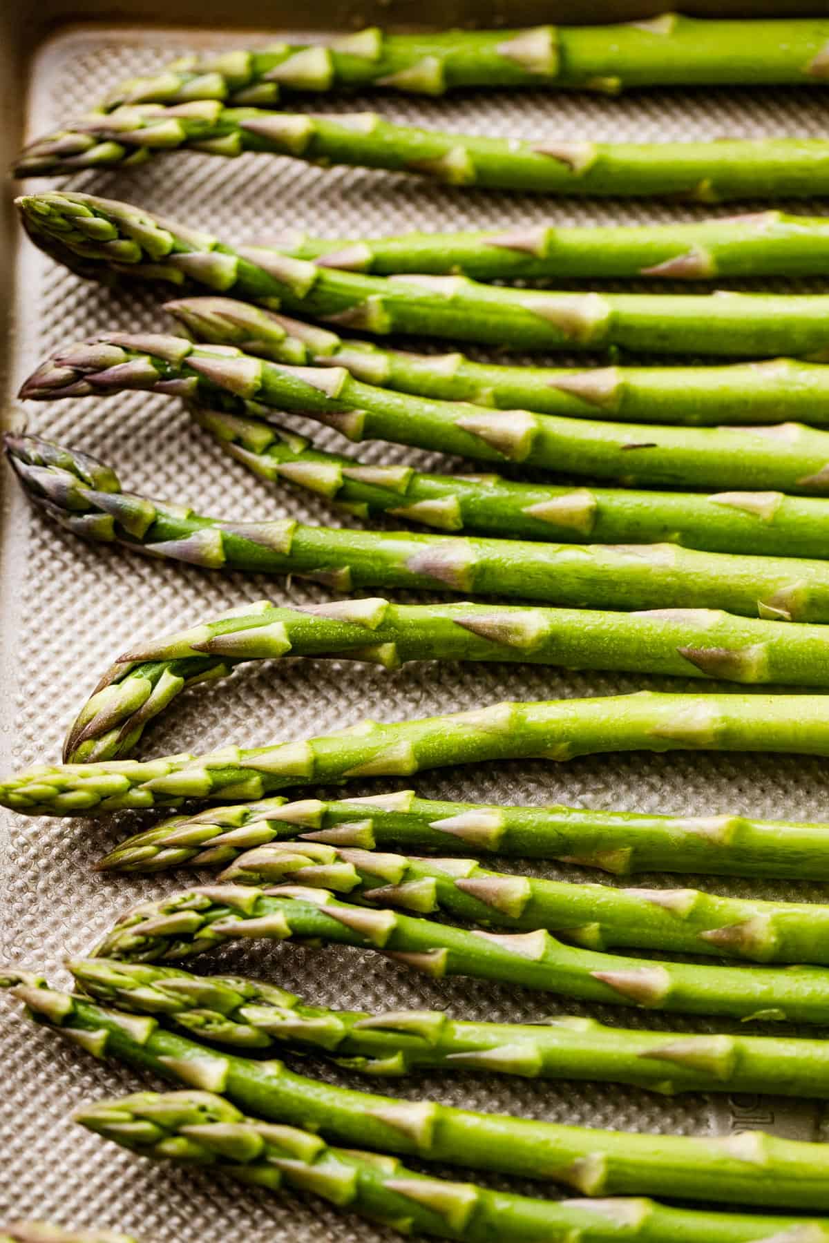 raw asparagus spears arranged on a baking sheet.