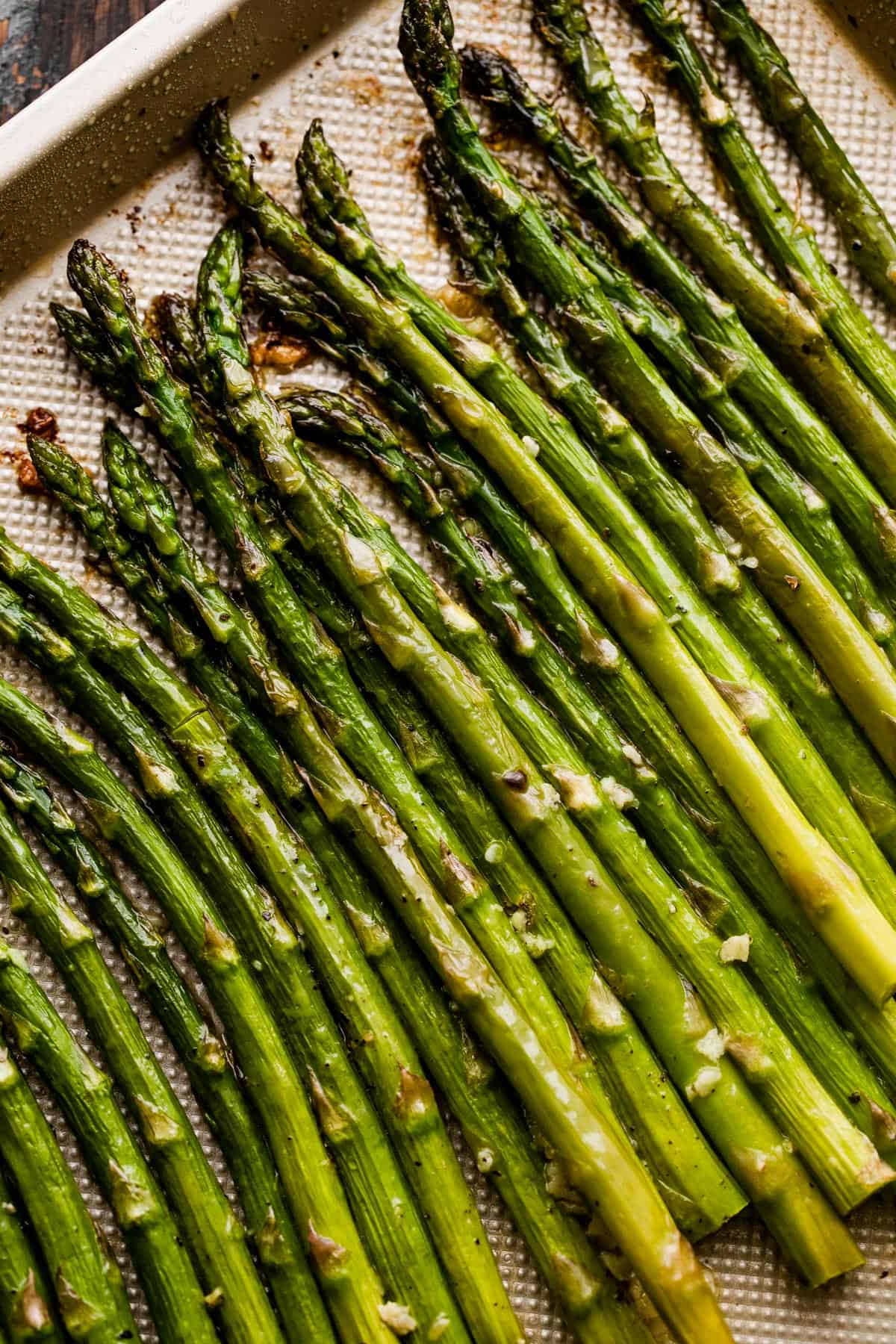 close up shot of asparagus spears arranged on a gold-colored baking sheet.