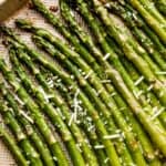 parmesan topped asparagus spears arranged on a gold-colored baking sheet.