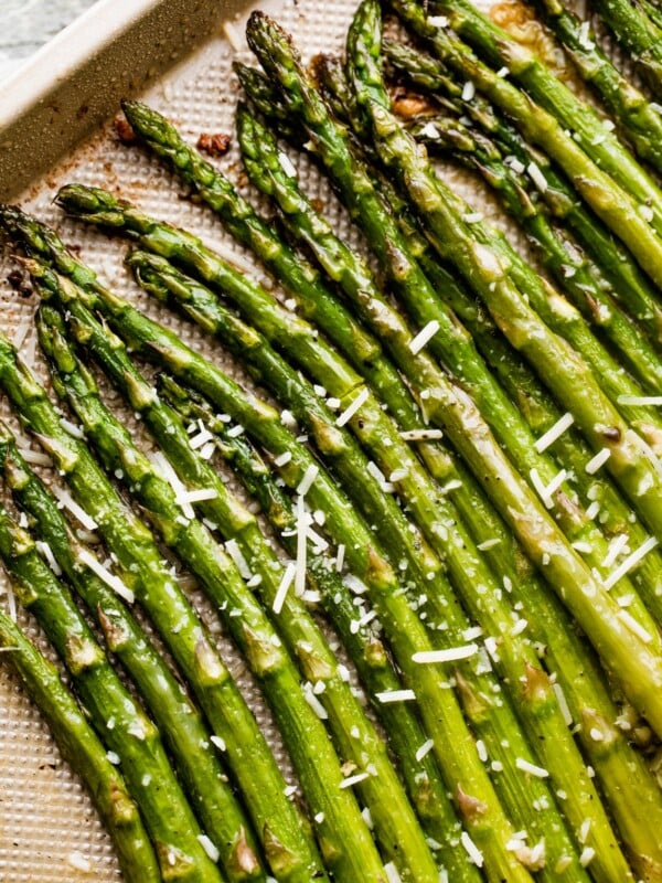 parmesan topped asparagus spears arranged on a gold-colored baking sheet.