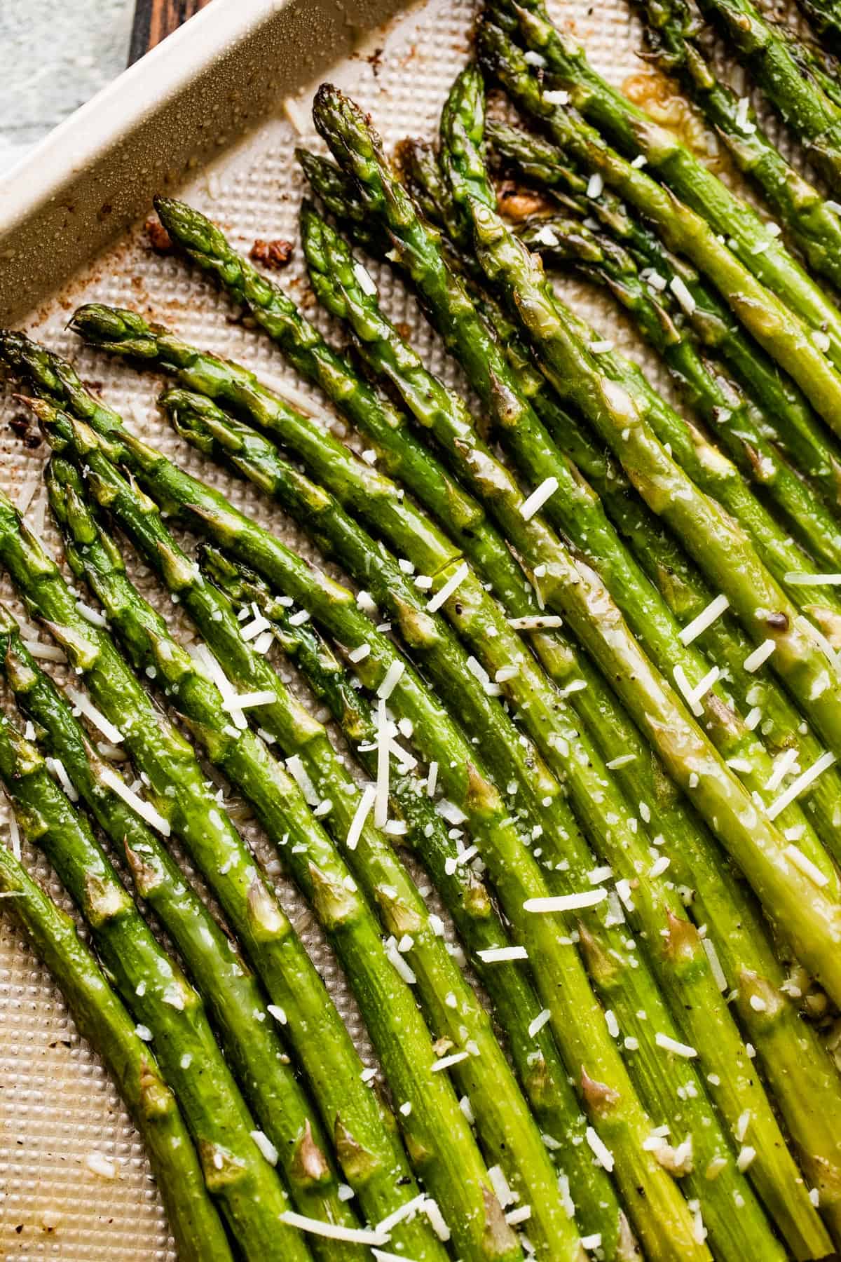 parmesan topped asparagus spears arranged on a gold-colored baking sheet.