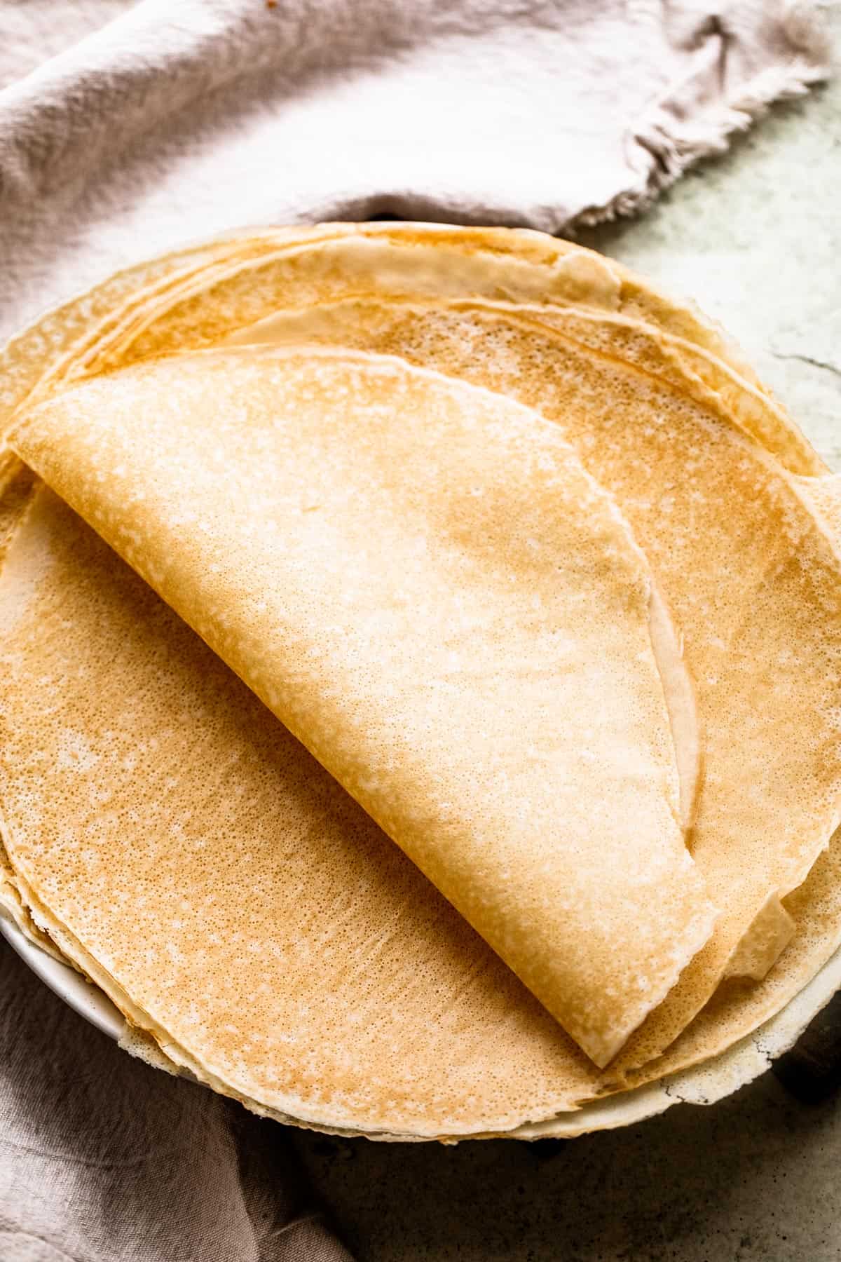 freshly made crepes set on a plate and half of the crepes folded over in half.